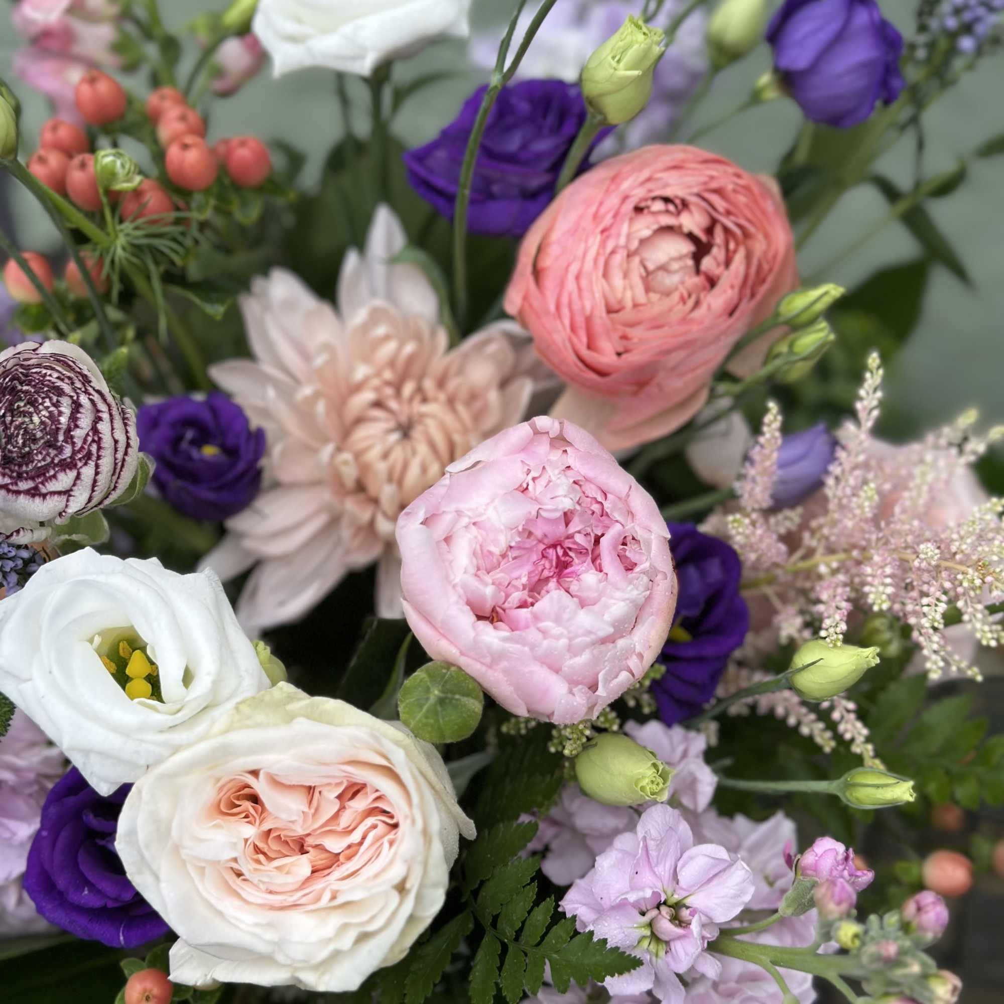 Arrangement of pink peonies, garden roses, and purple lisianthus in a white vase