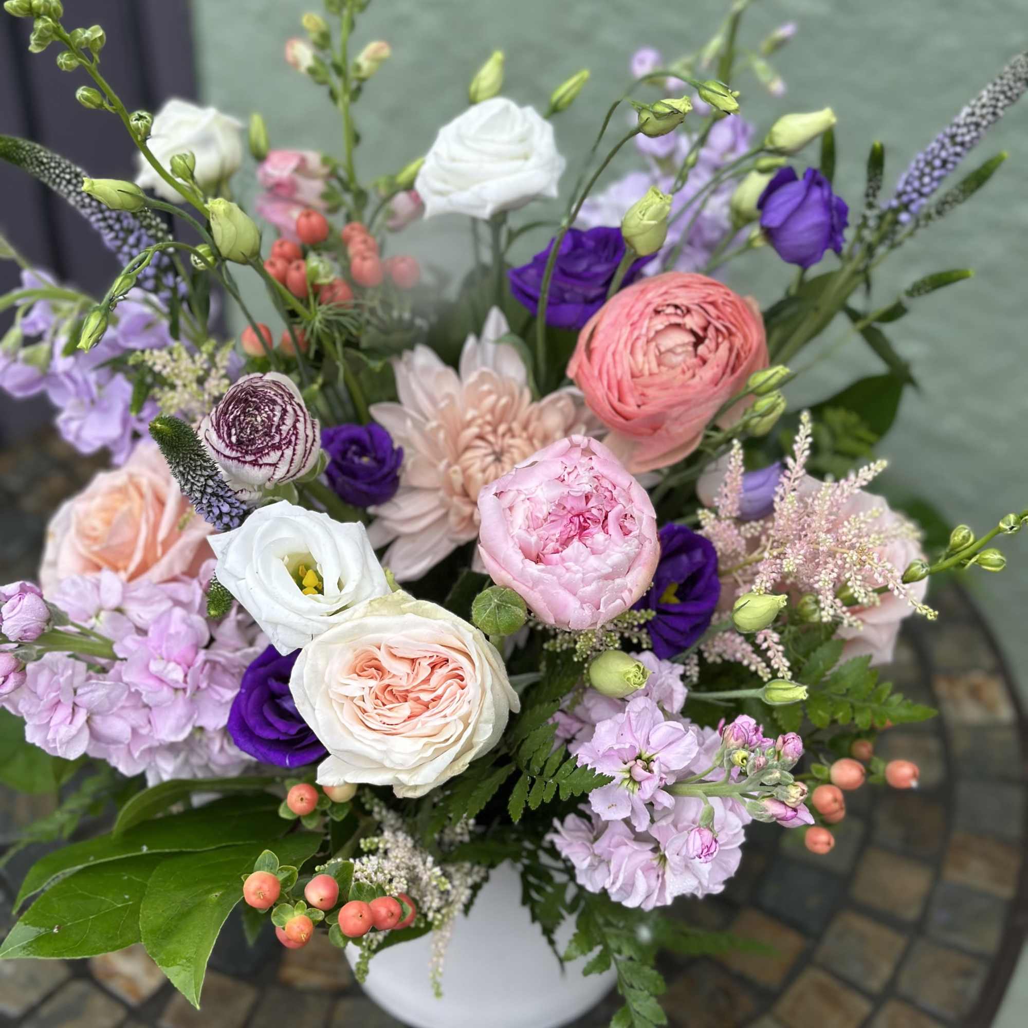 Garden-style arrangement of pink, white, and purple blooms in a white bowl vase on a mosaic table