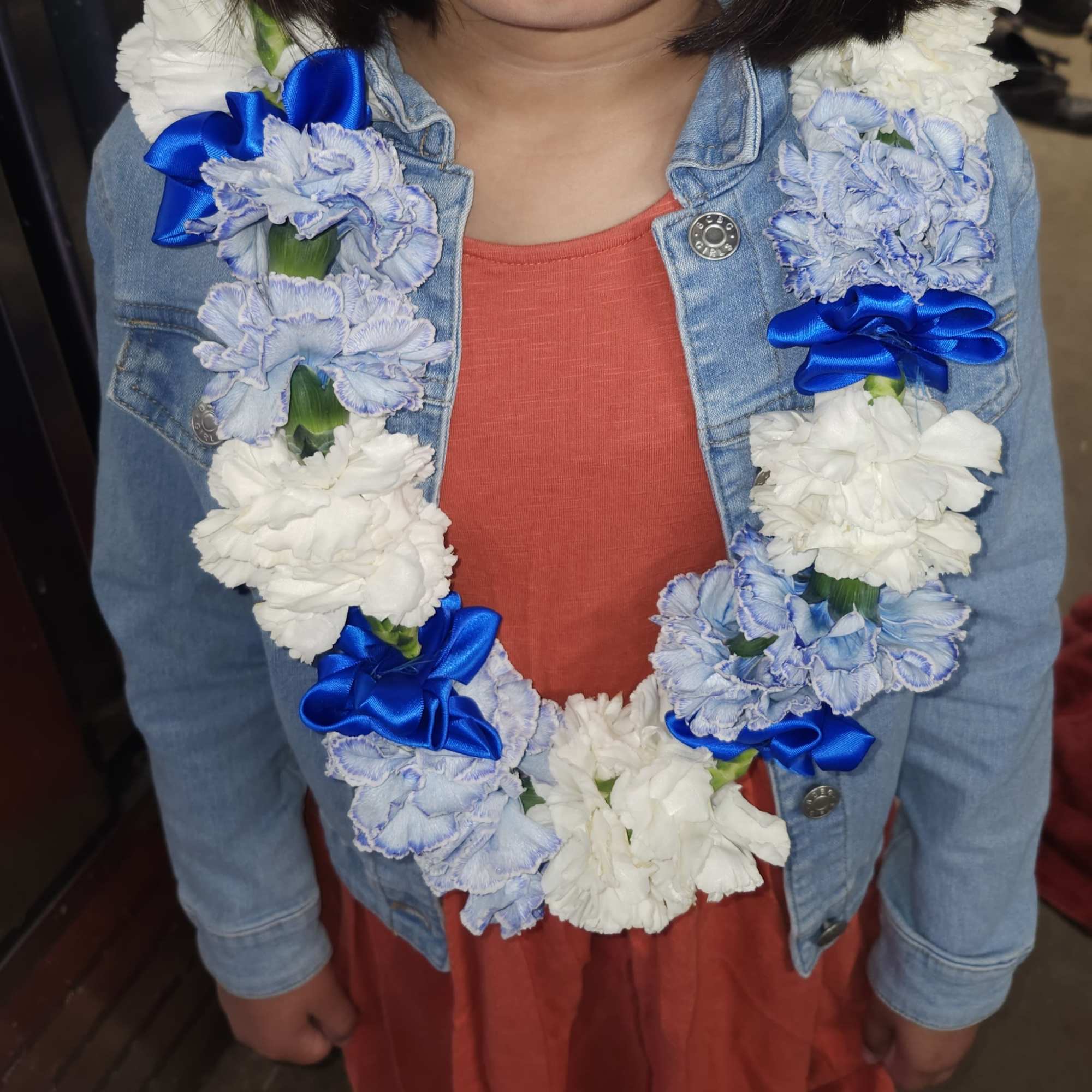 Flower lei with blue and white carnations worn over a denim jacket