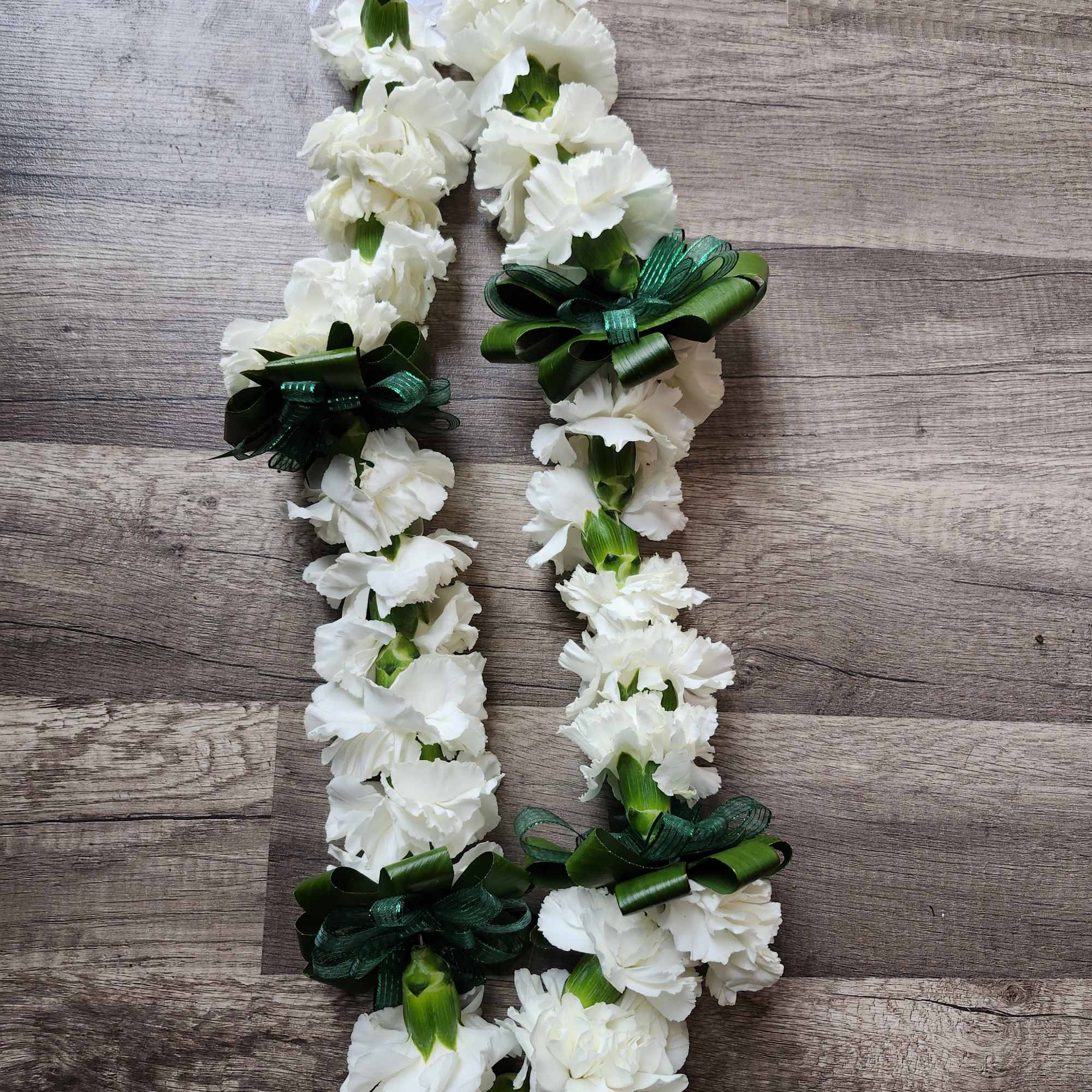 White carnation lei with green ribbon bows on a wood surface