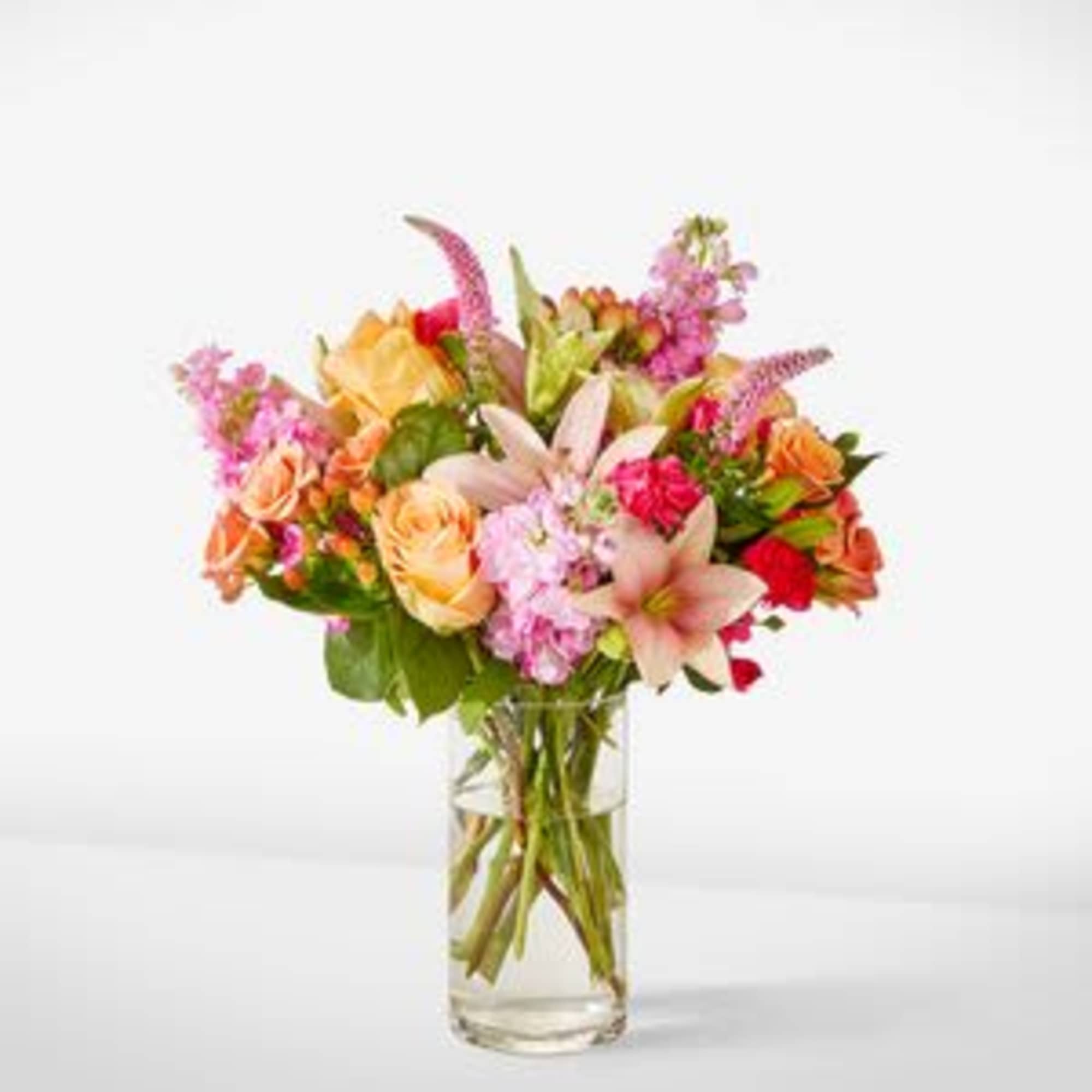 Mixed bouquet of pink, peach, and orange flowers in a clear glass vase