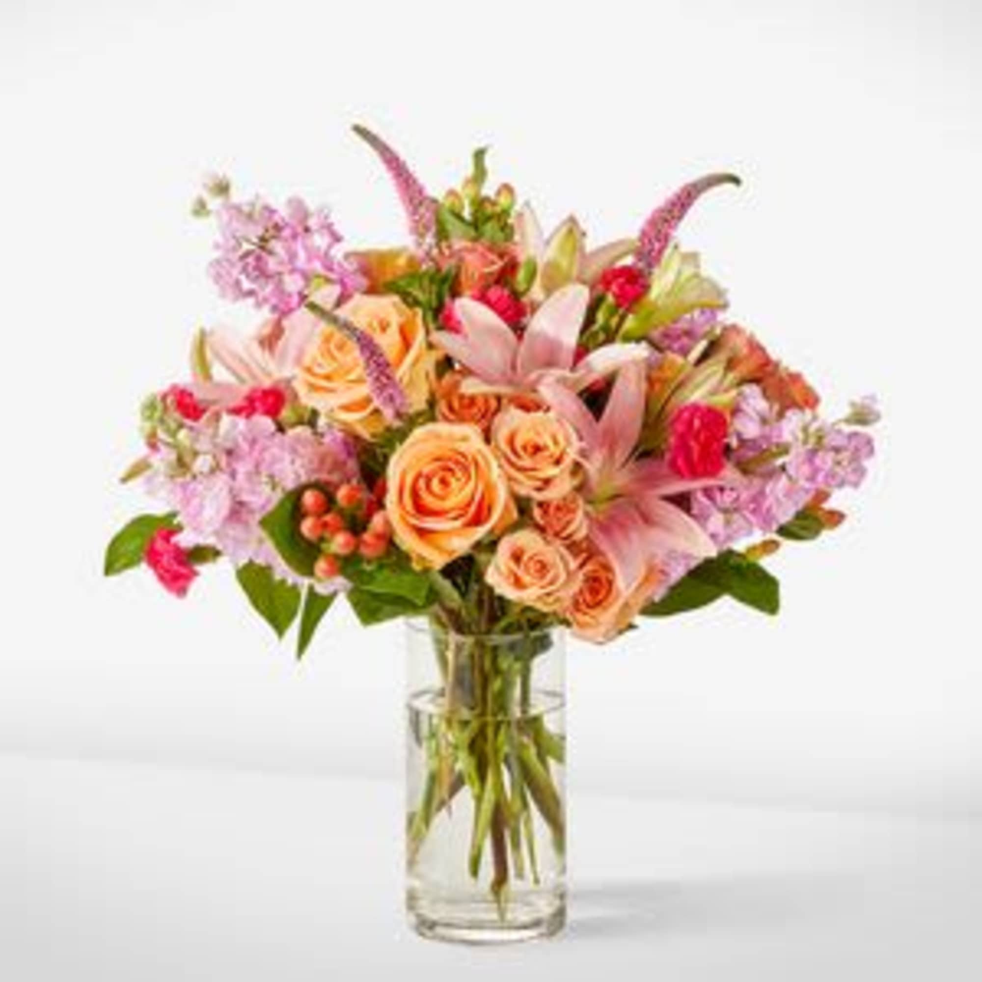 Mixed bouquet of pink and peach flowers in a clear glass vase