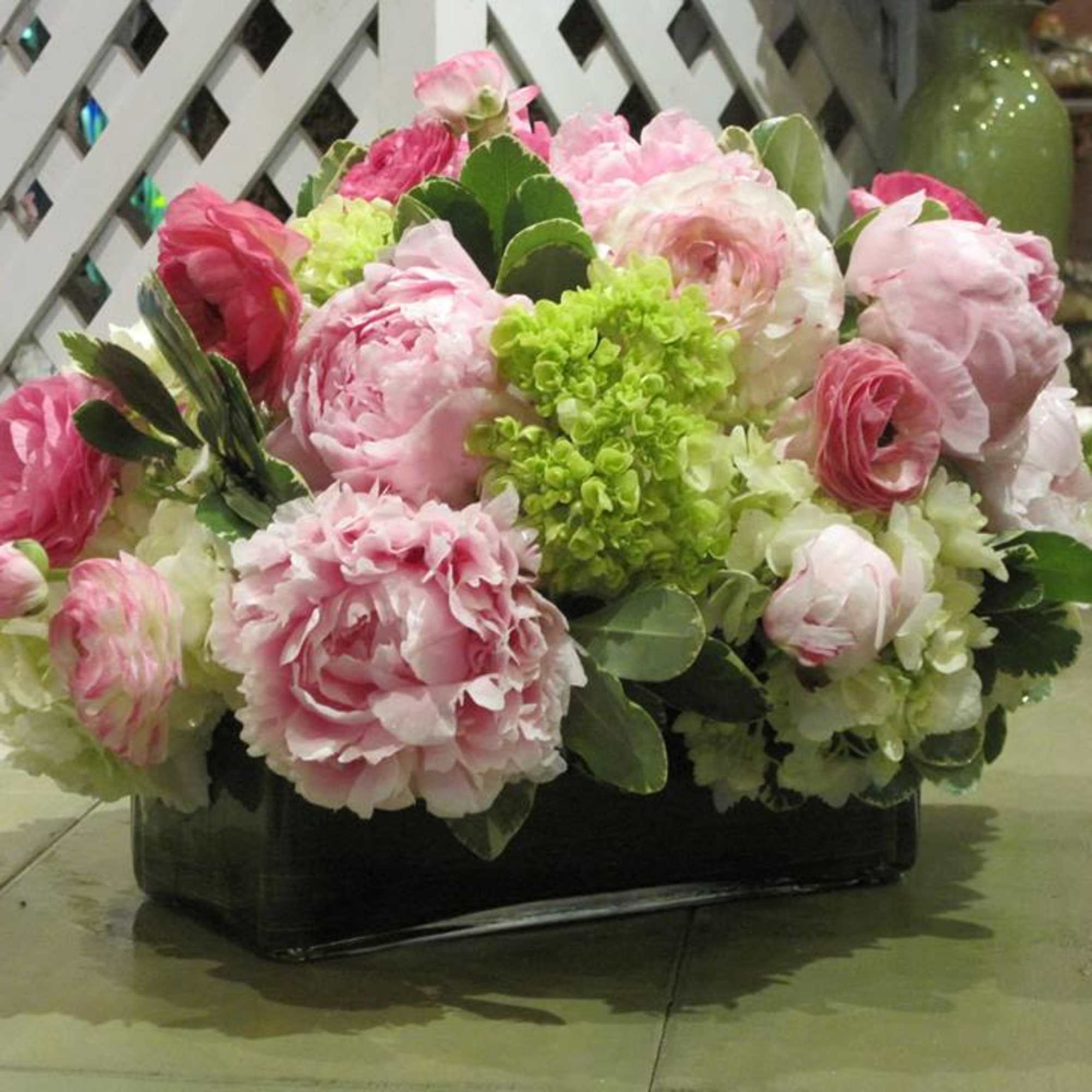 Low rectangular arrangement of pink peonies, white hydrangeas, and green blooms in a glass vase