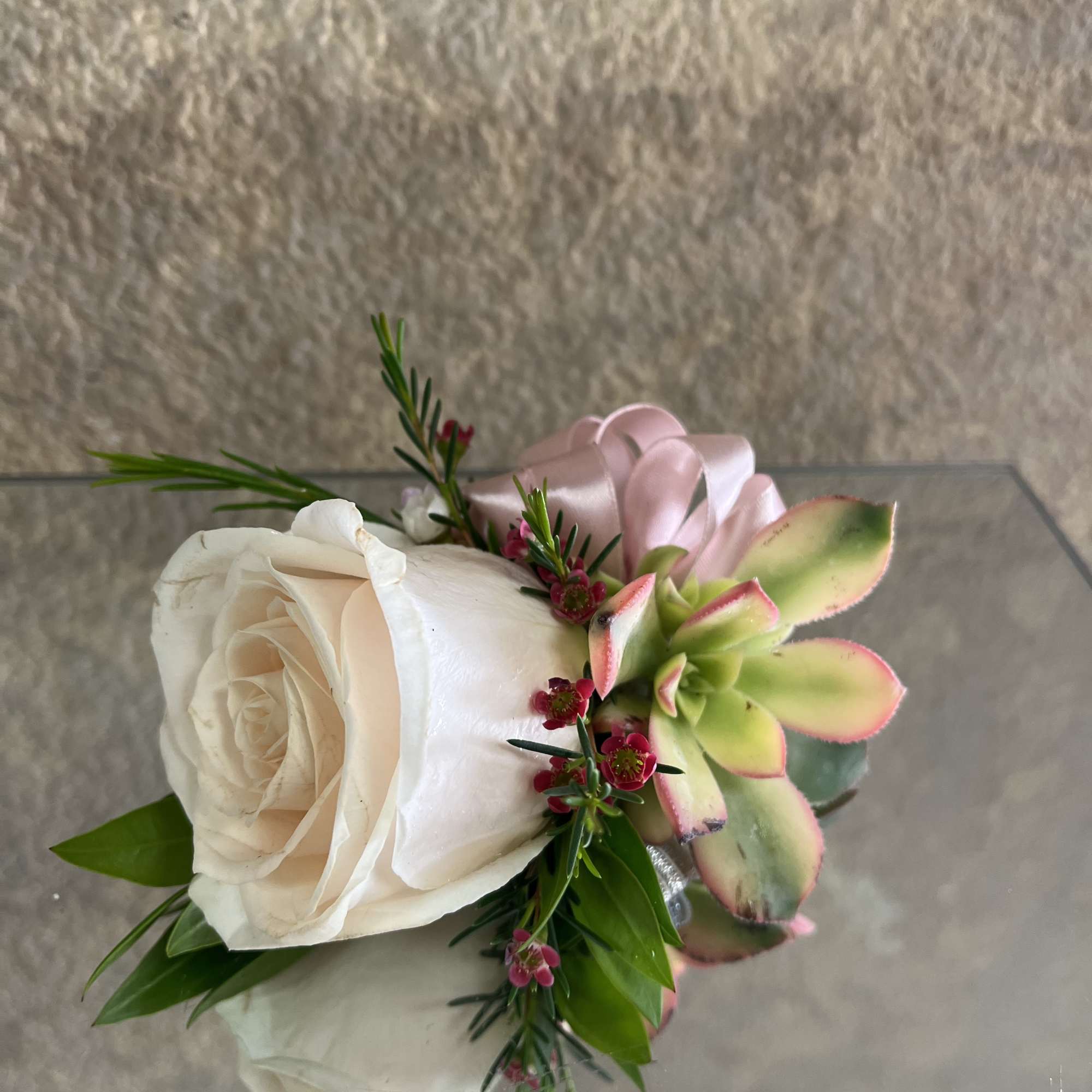 Small ivory rose and succulent corsage with pink ribbon and tiny red blooms.