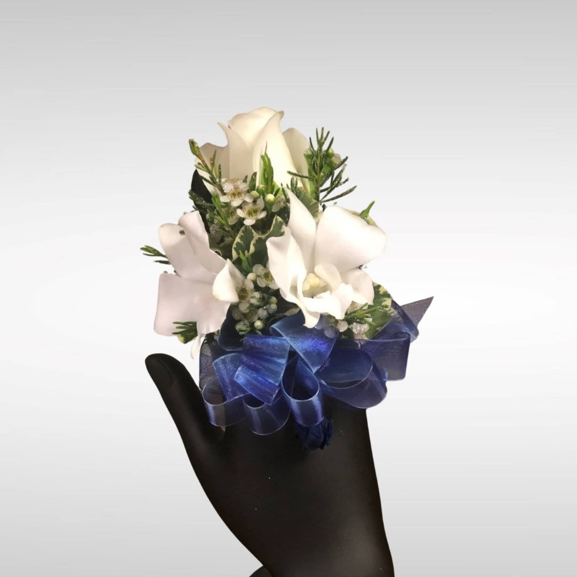 White rose wrist corsage with small white blooms and blue ribbon on a display hand