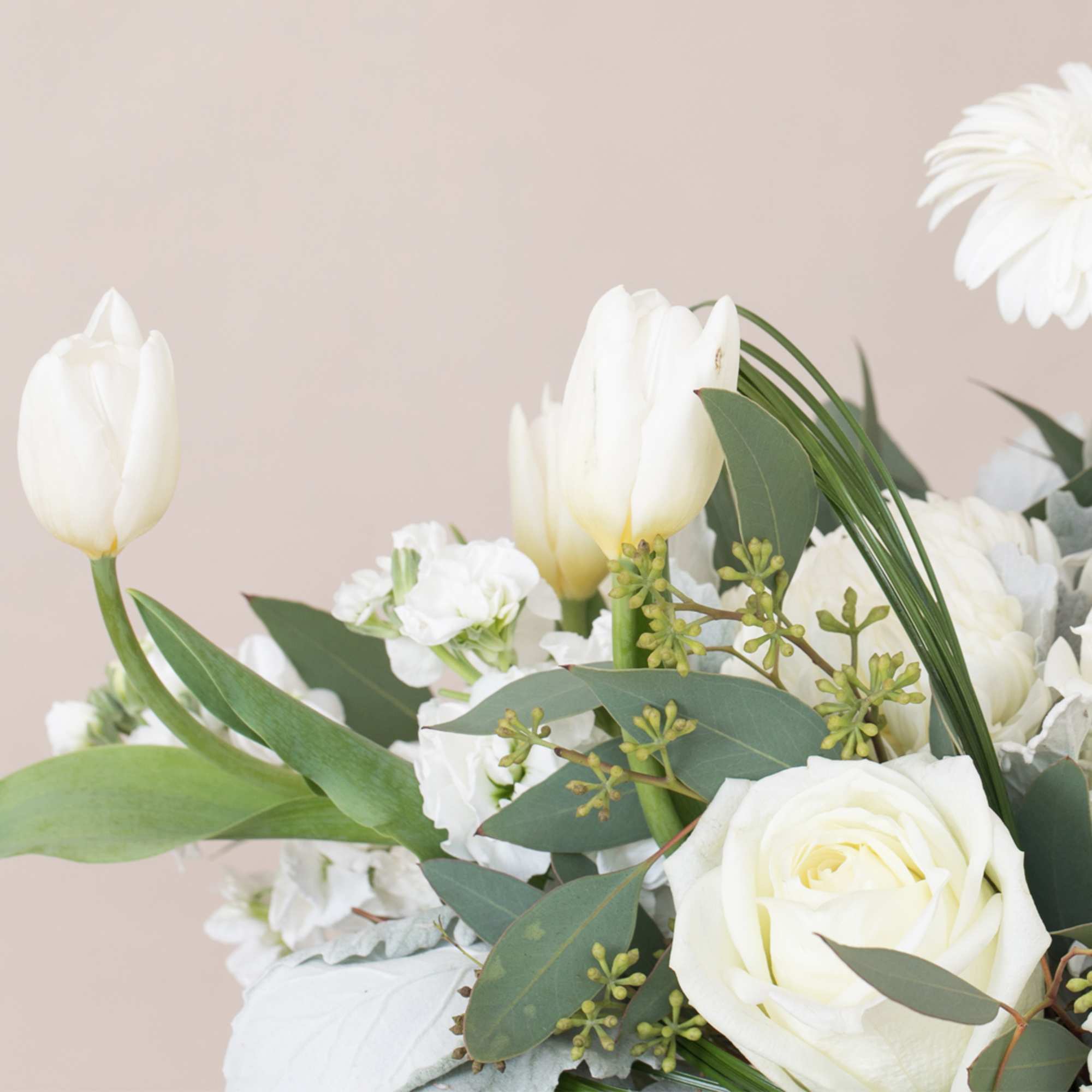 White tulips, roses, and other white blooms with green accents in a soft neutral arrangement