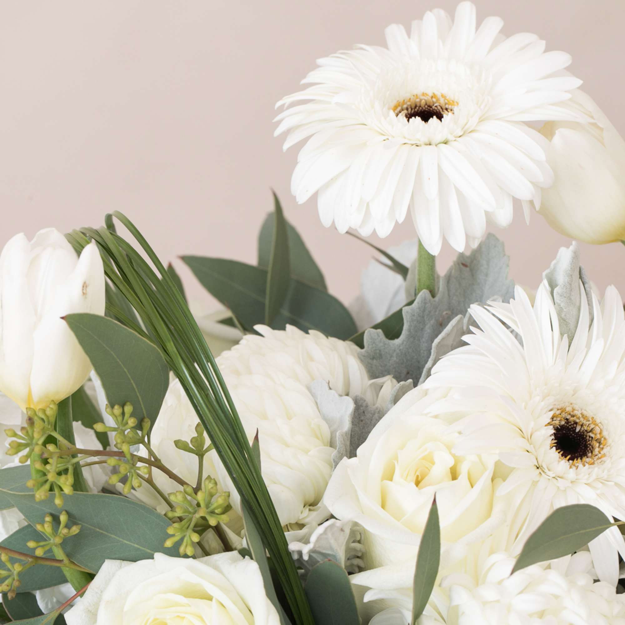 White bouquet with gerbera daisies, roses, tulips, and chrysanthemums on a neutral background