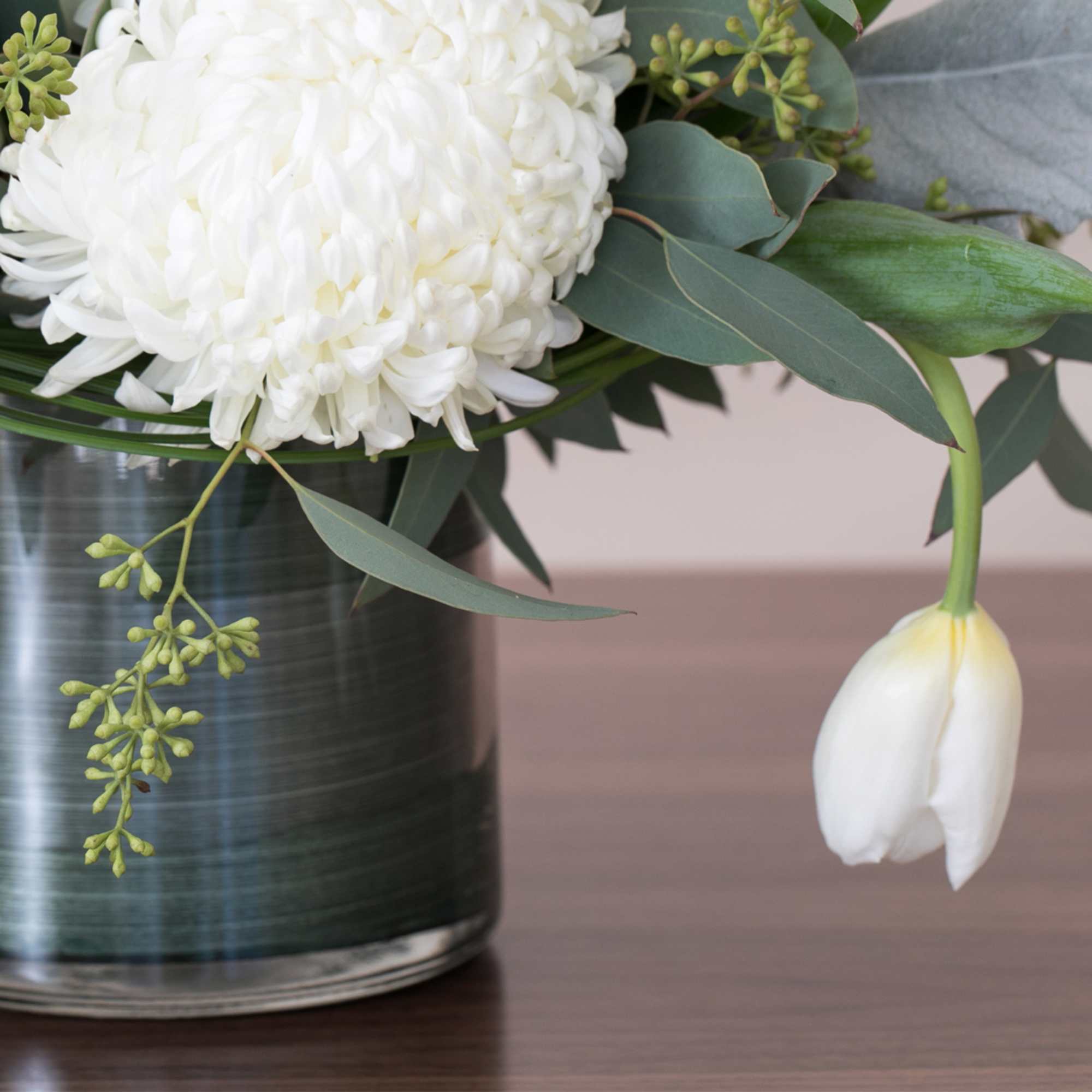 Low arrangement of white chrysanthemum and tulip in a clear glass vase on a wooden surface