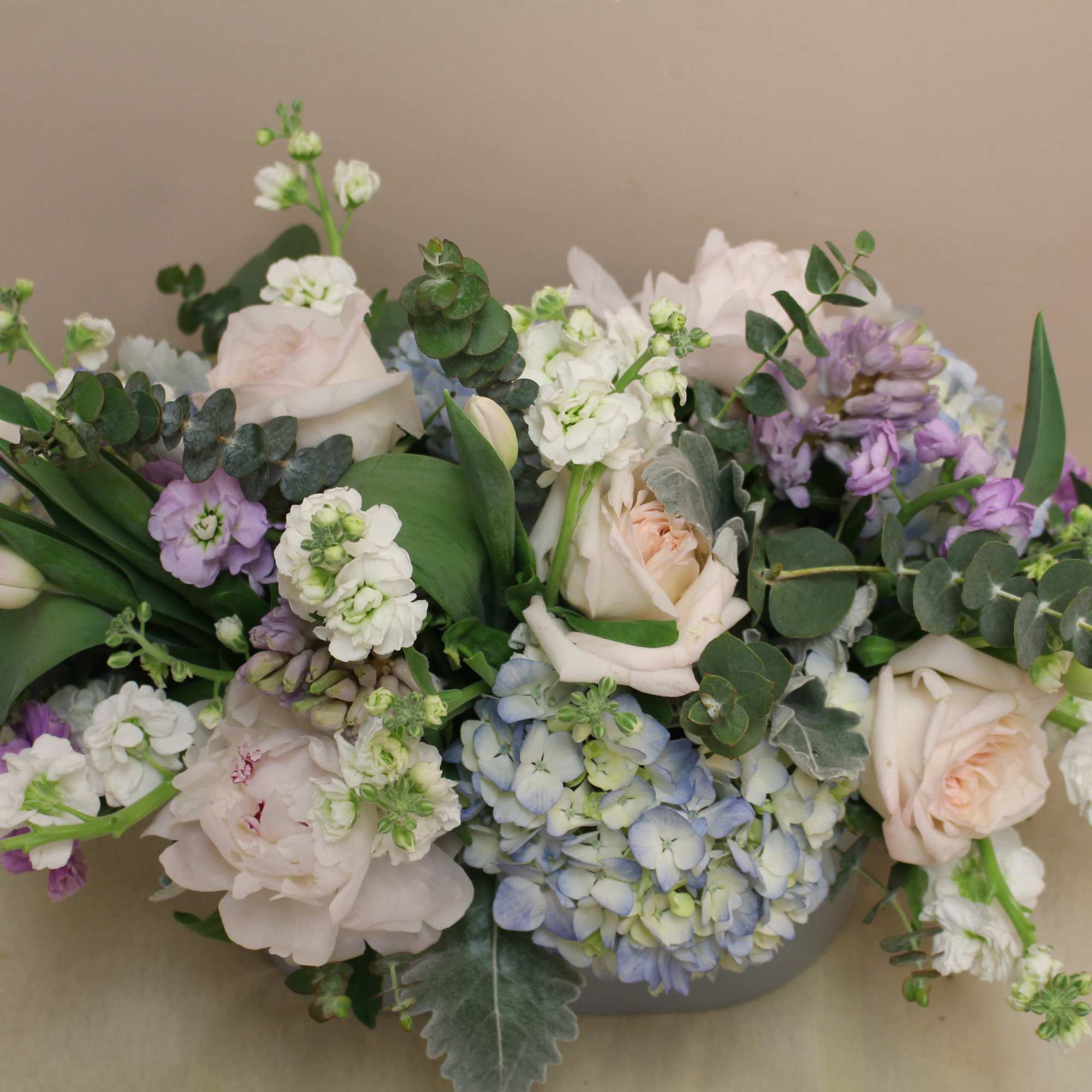 Low floral arrangement with pale roses, blue hydrangea, and white blooms in a vase