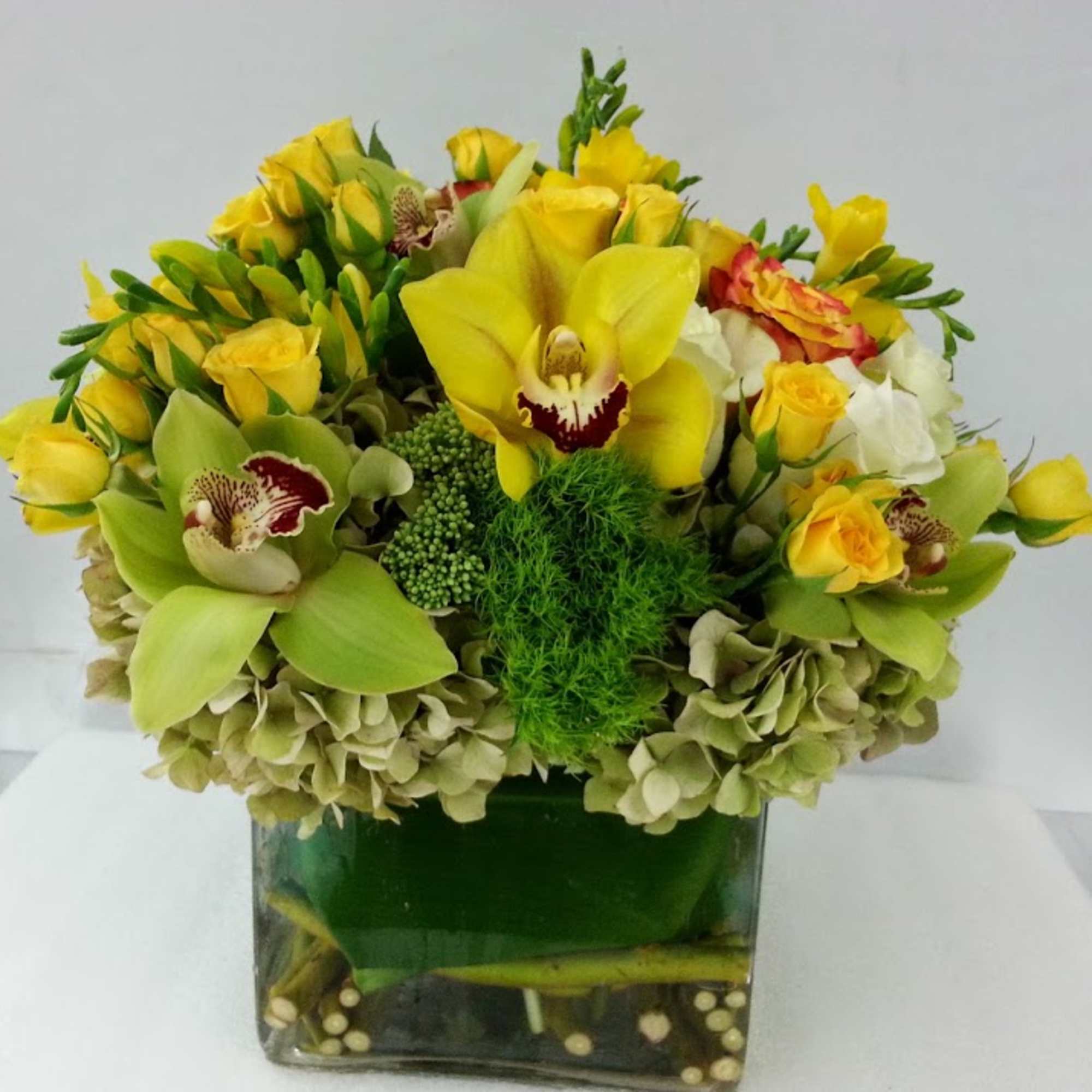 Yellow orchids and roses arranged in a square glass vase