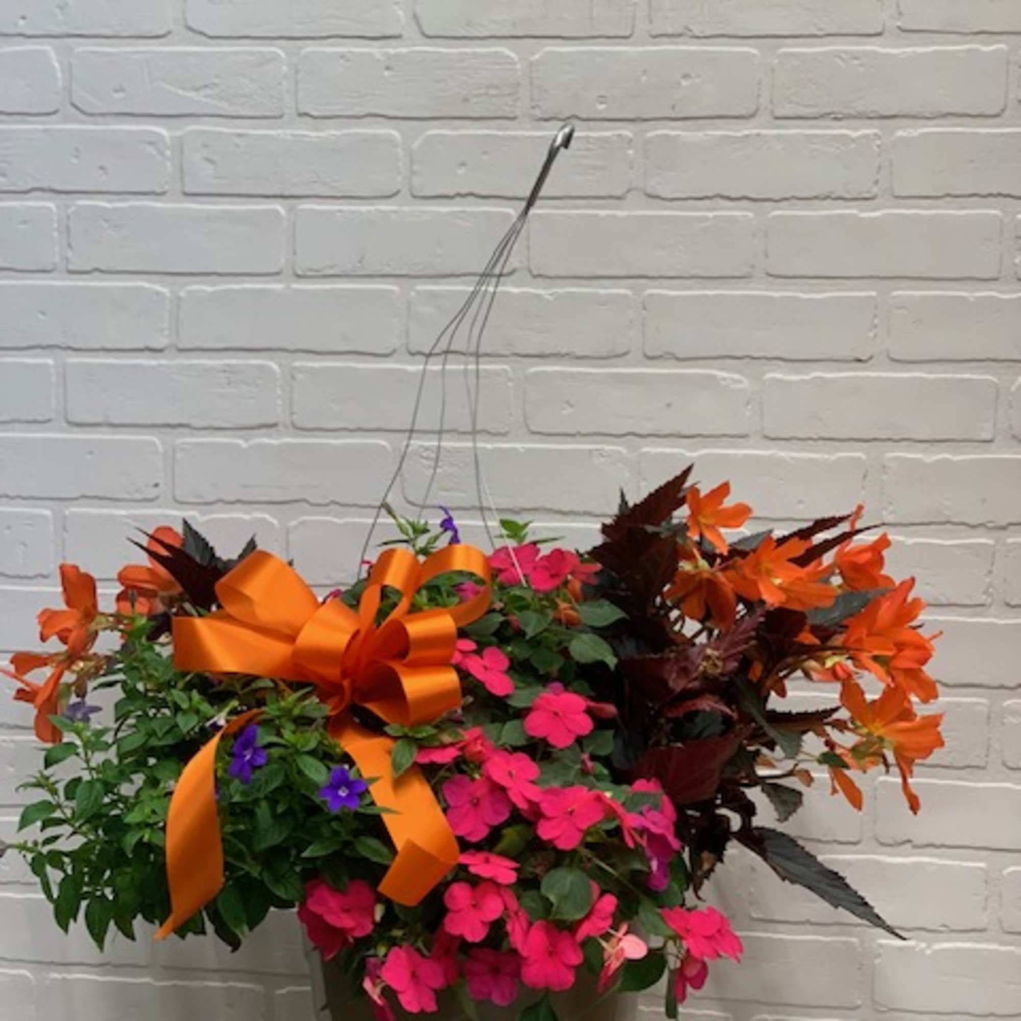 Hanging basket of pink and orange flowers with a large orange bow