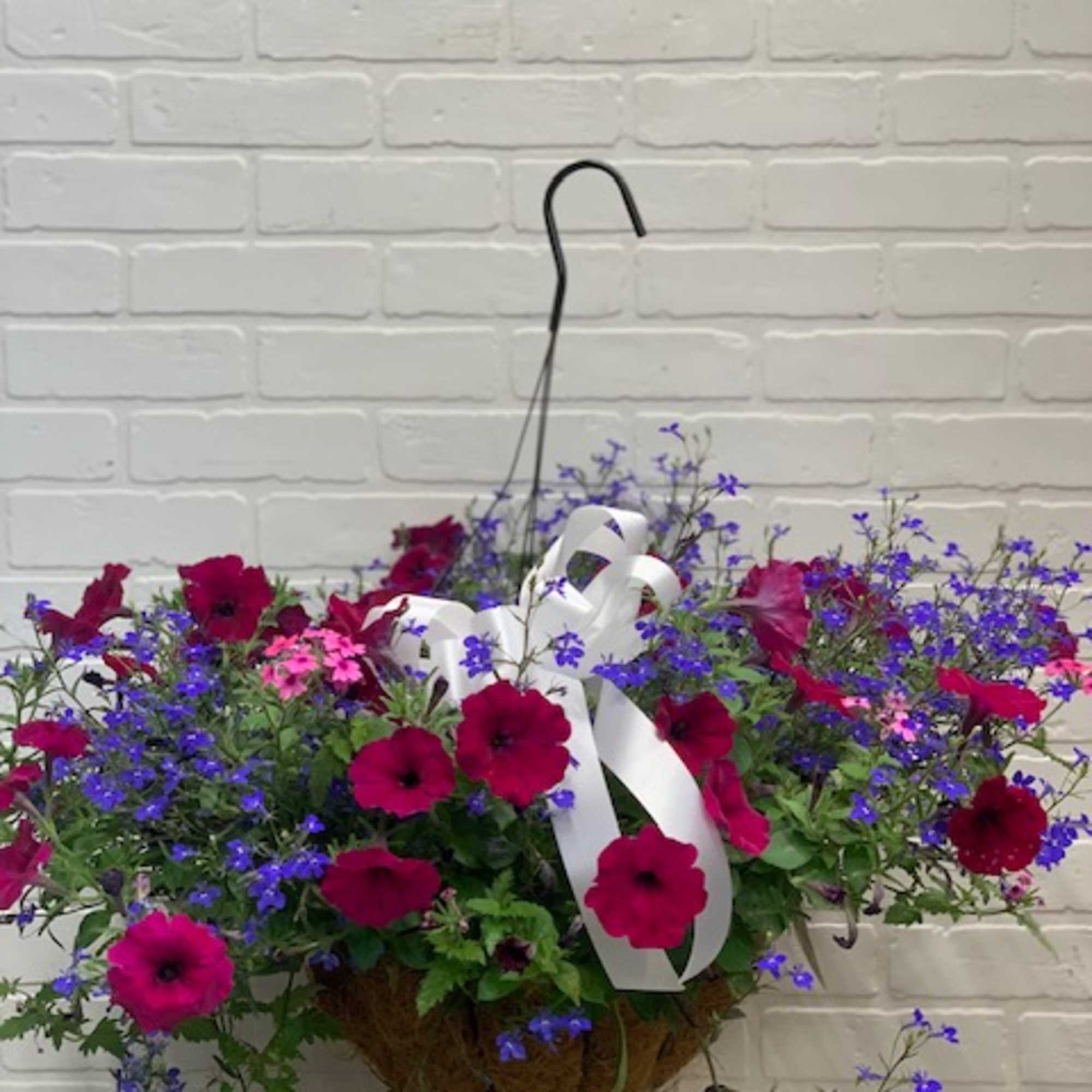 Hanging basket of magenta and purple flowers with a white ribbon