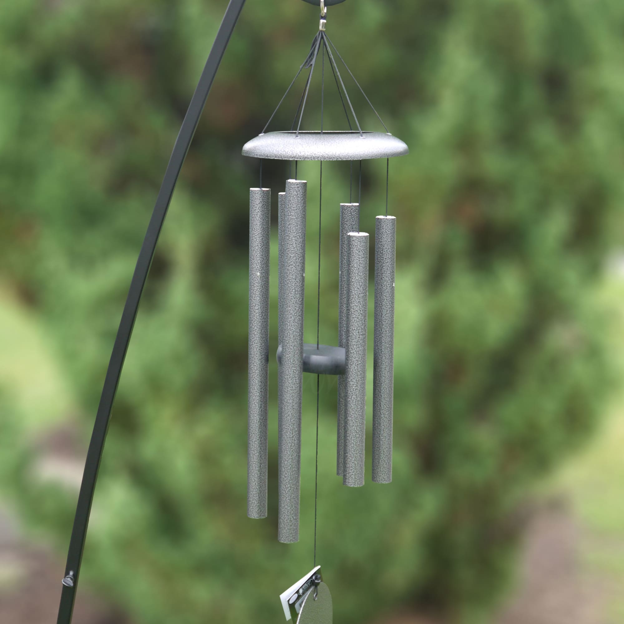 Silver wind chime hanging from a black metal hook outdoors
