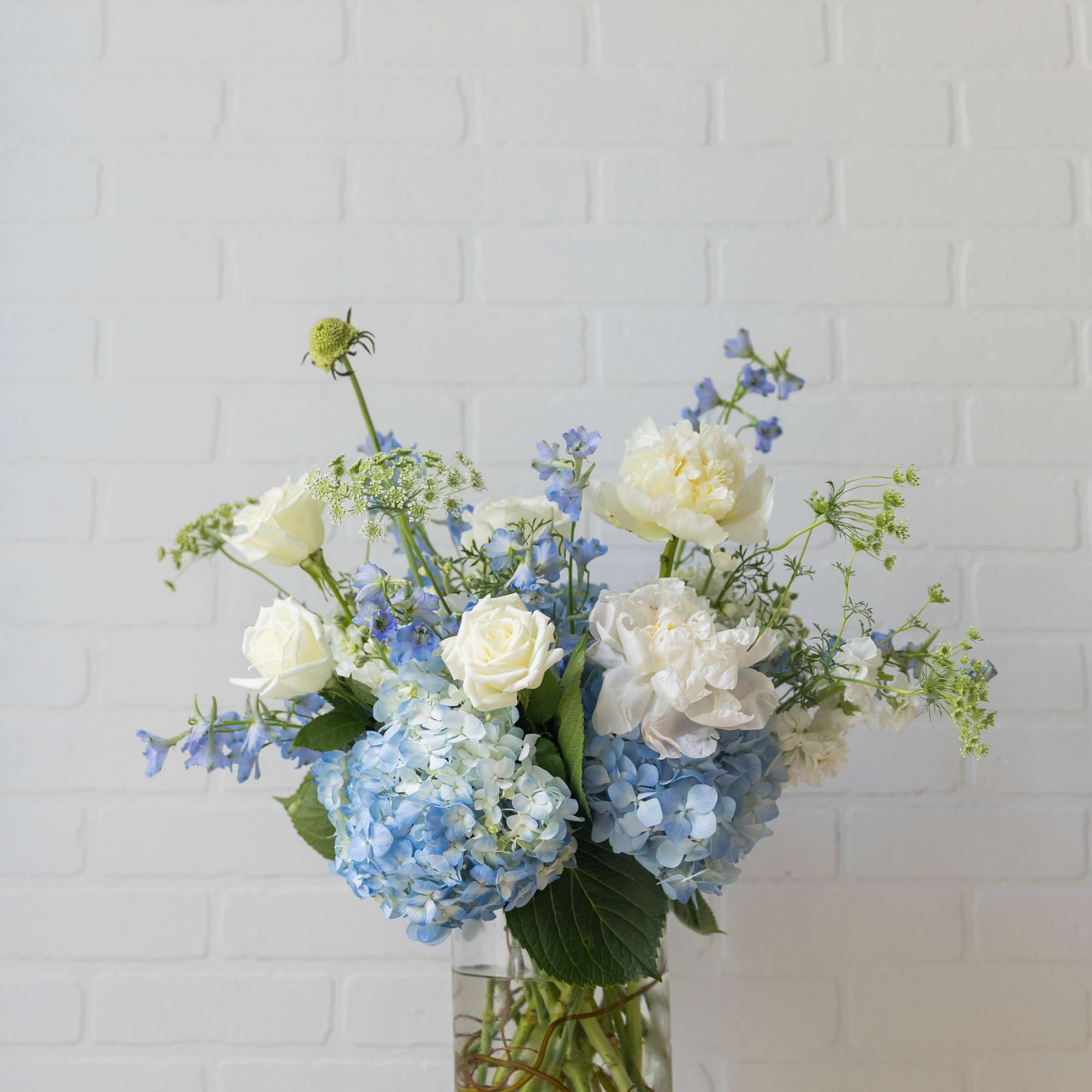 A soft, garden-inspired arrangement in calming blue and ivory tones, featuring lush