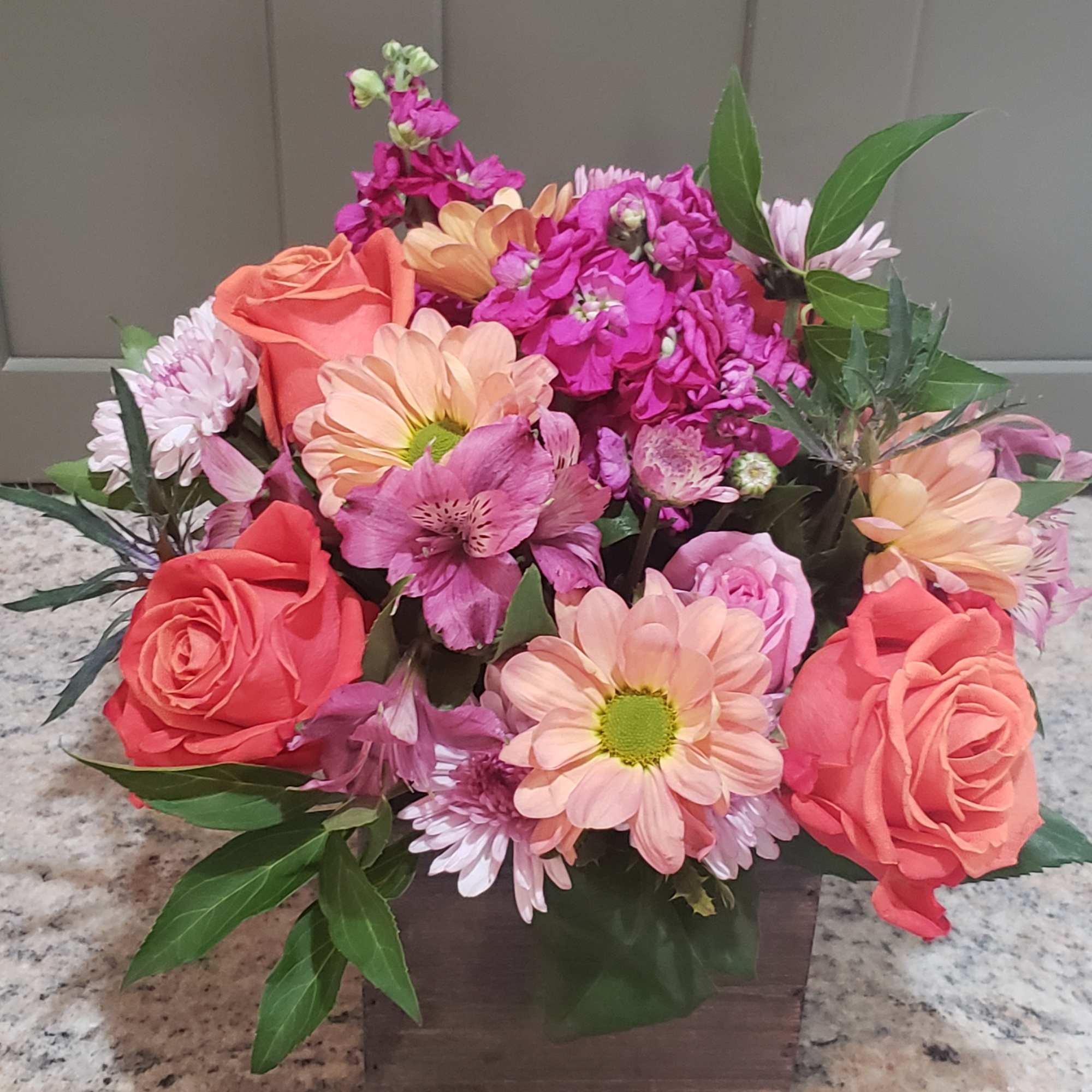 Compact arrangement of pink, peach, and coral flowers in a rustic wooden box.