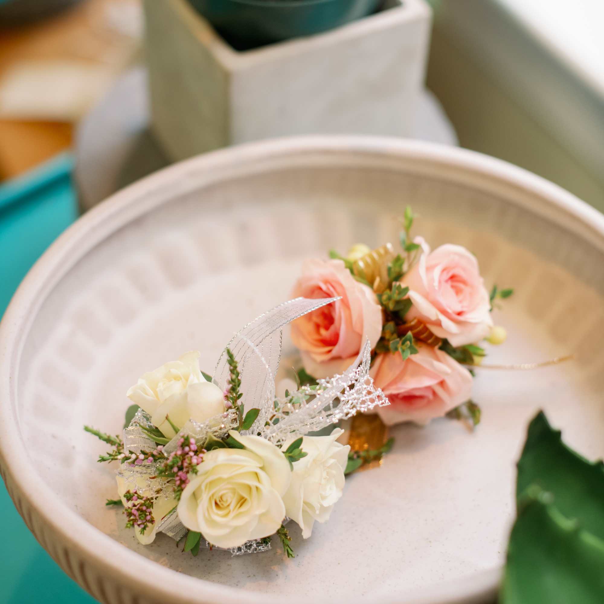 Two small floral corsages with cream and blush roses in a shallow dish