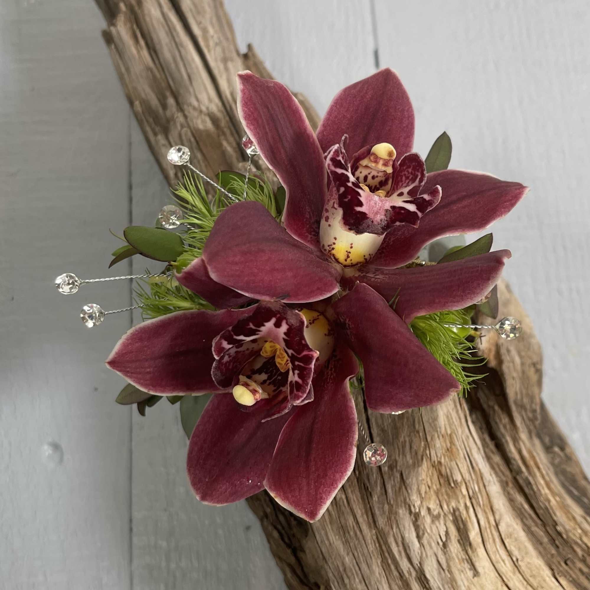 Two deep burgundy orchid blooms with decorative accents on driftwood