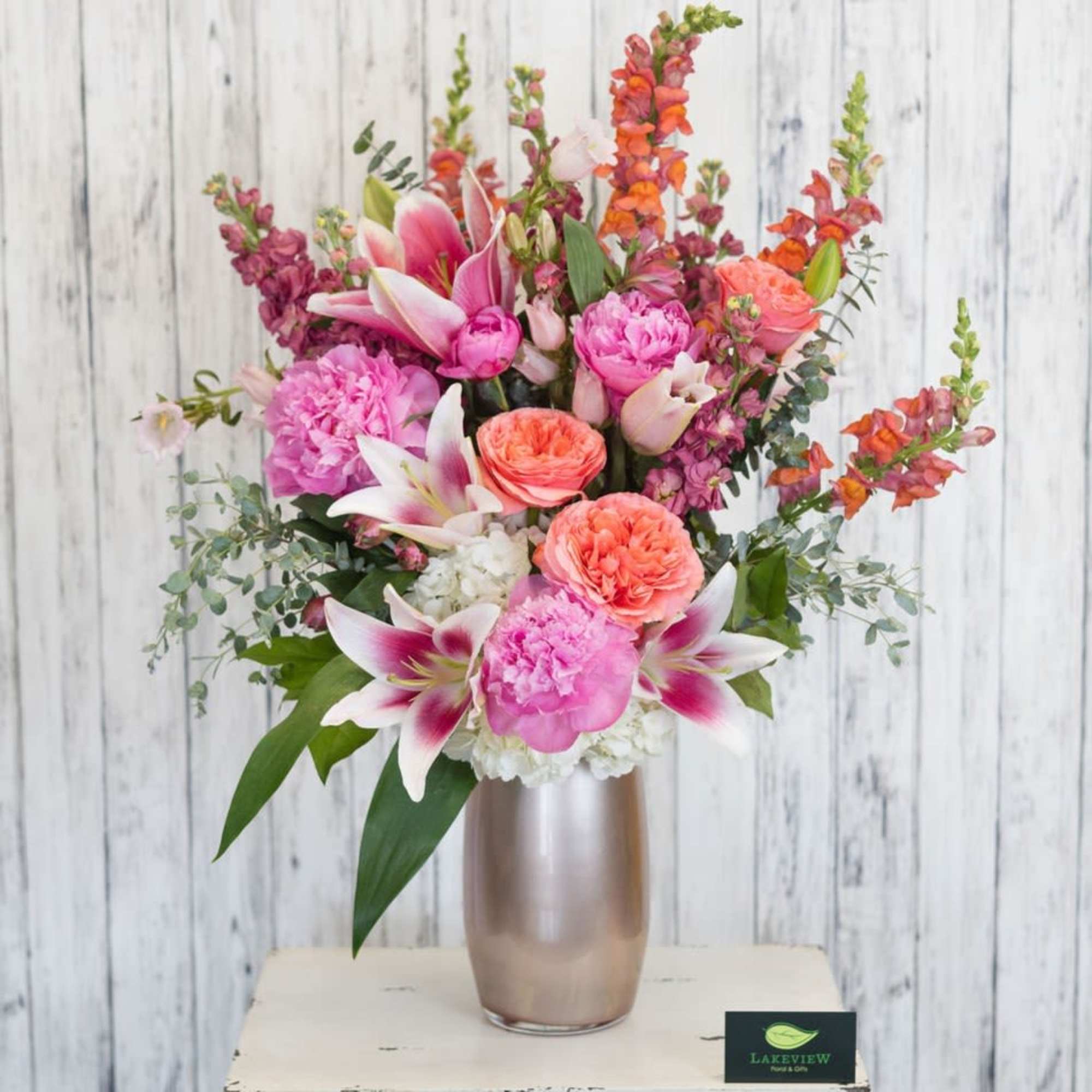 A striking, garden-style arrangement bursting with peach, orange, pink, white and touches
