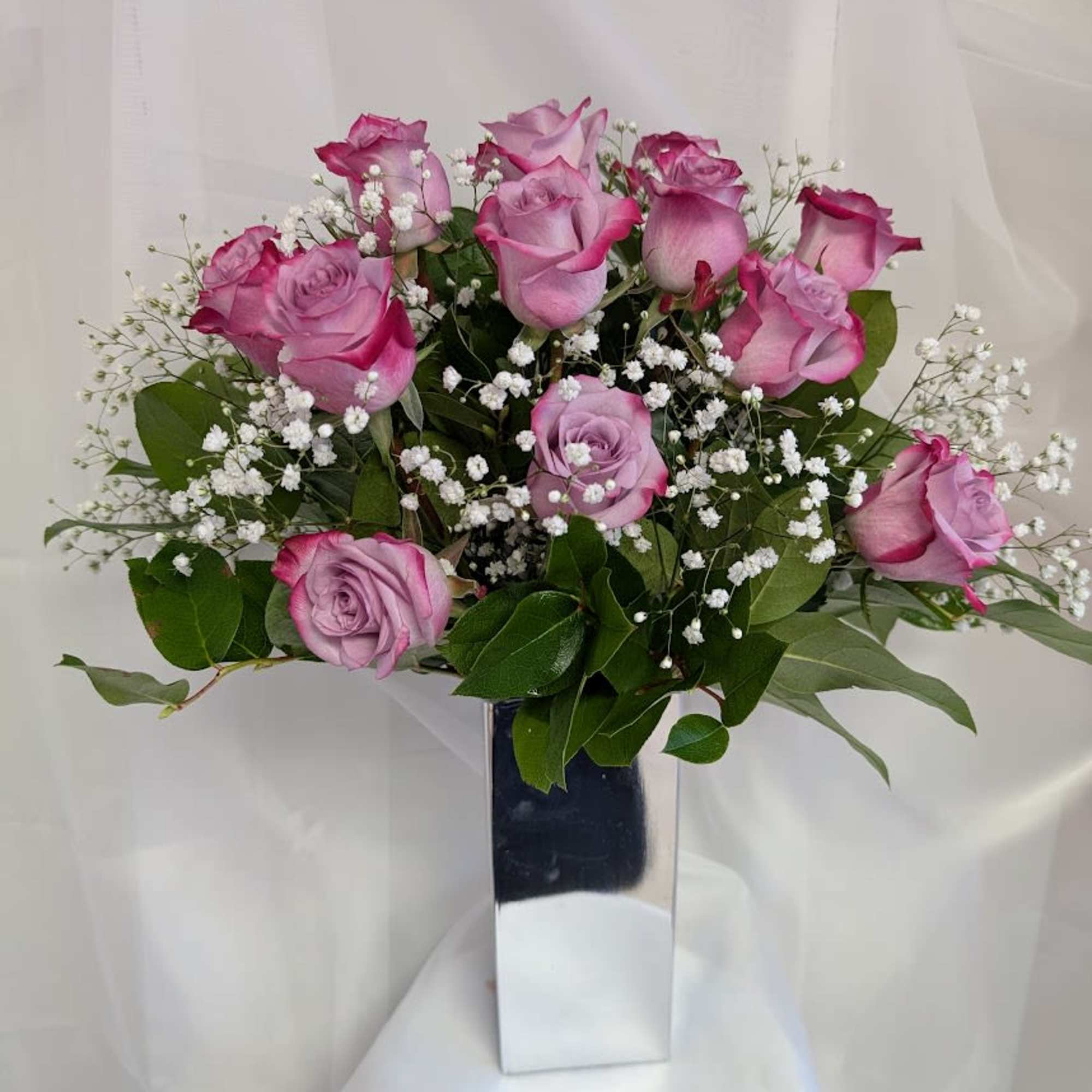 12 Deep purple roses complimented by baby's breath and foliage.