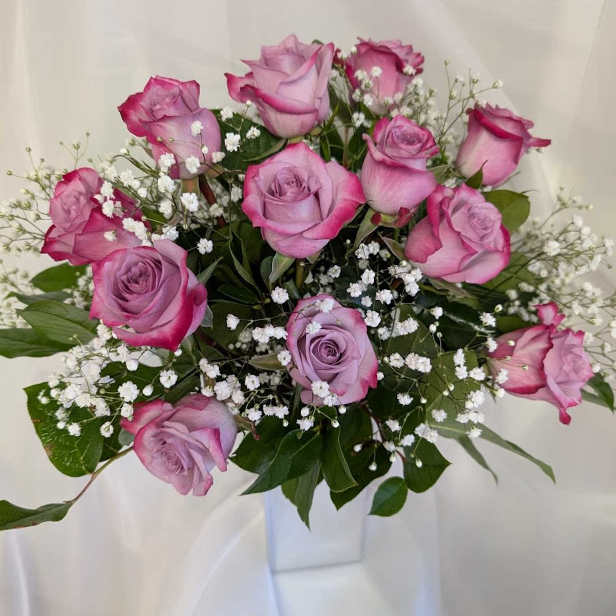 12 Deep purple roses complimented by baby's breath and foliage.