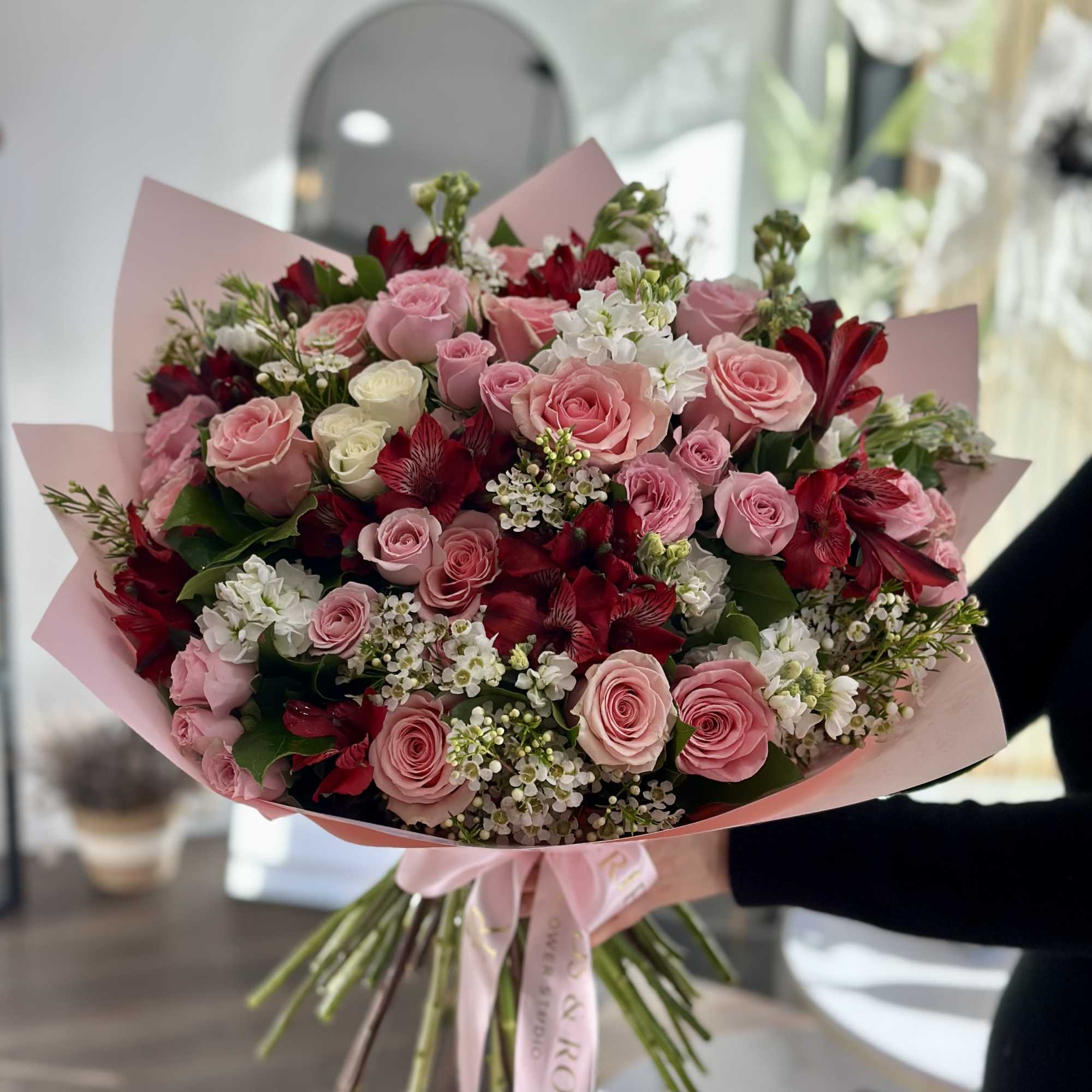Bouquet of pink and red roses with white filler flowers wrapped in pink paper
