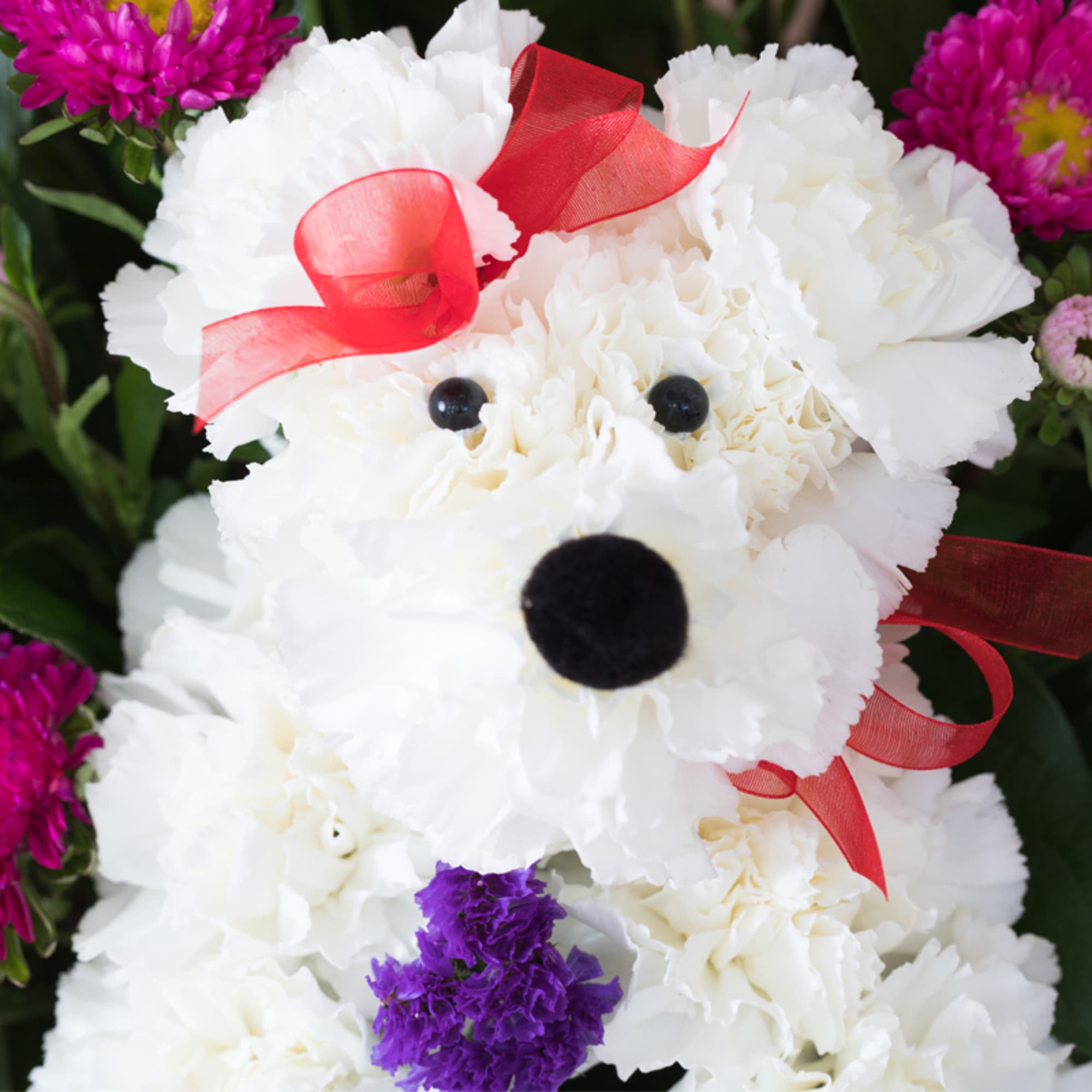Dog-shaped arrangement of white carnations with red ribbon and purple and pink accent flowers