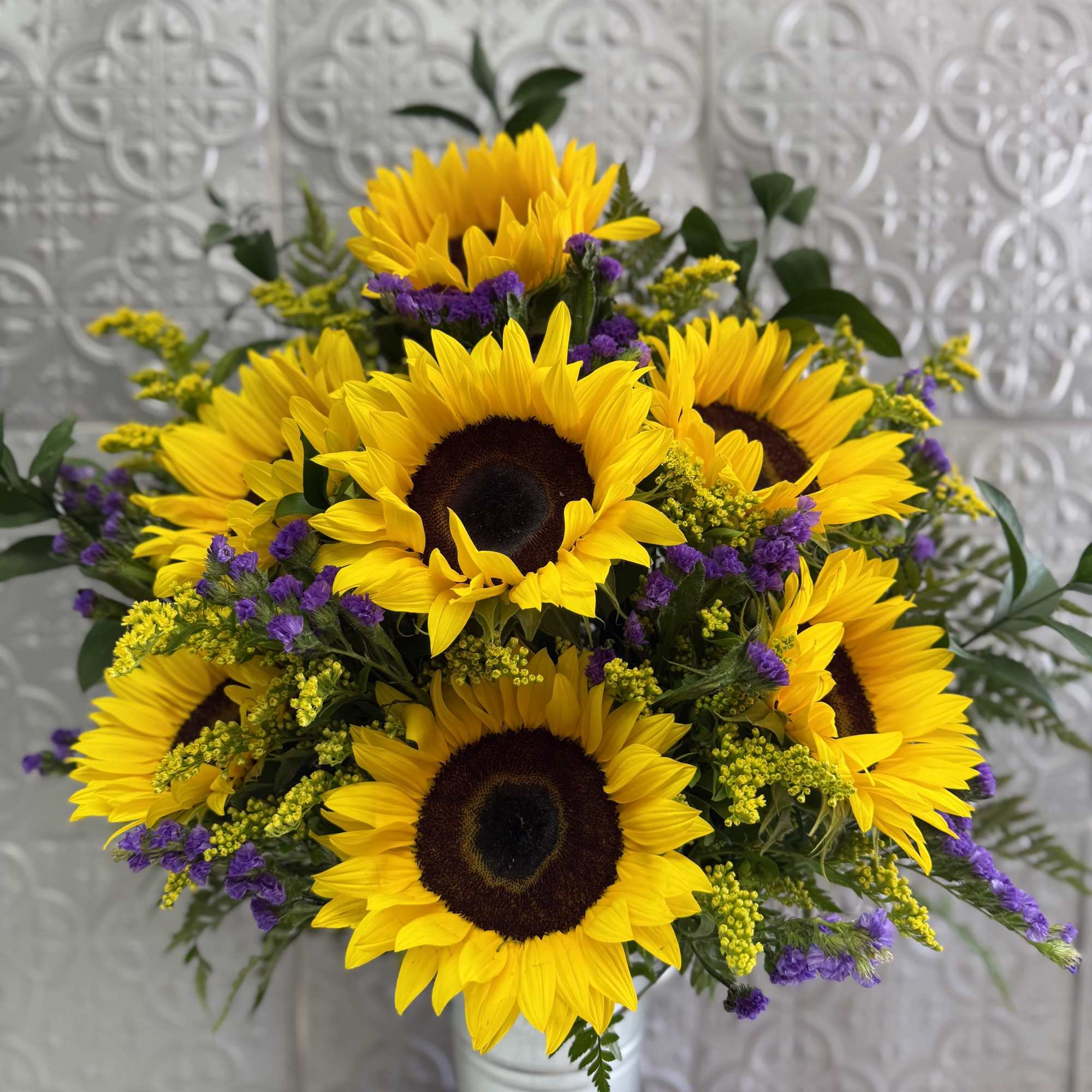 Bouquet of yellow sunflowers with purple filler in a white vase
