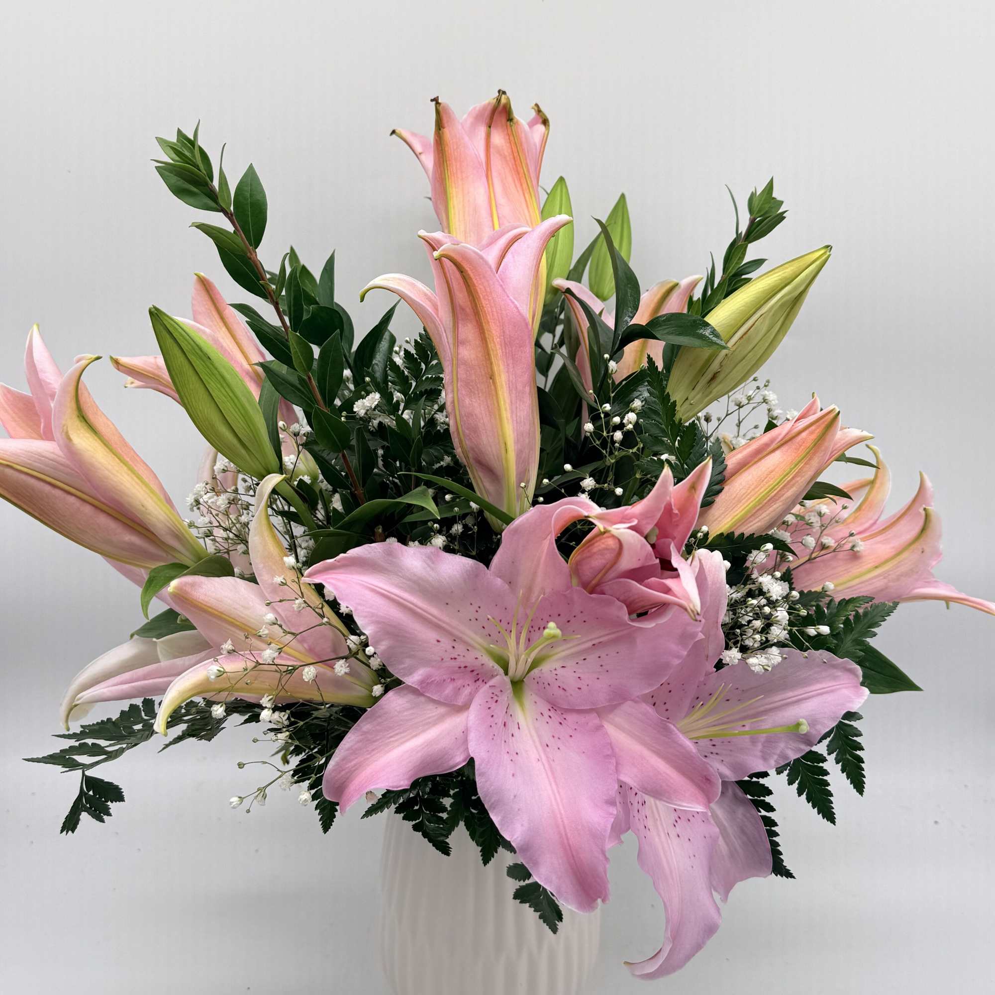 Pink lilies arranged in a white vase with baby's breath