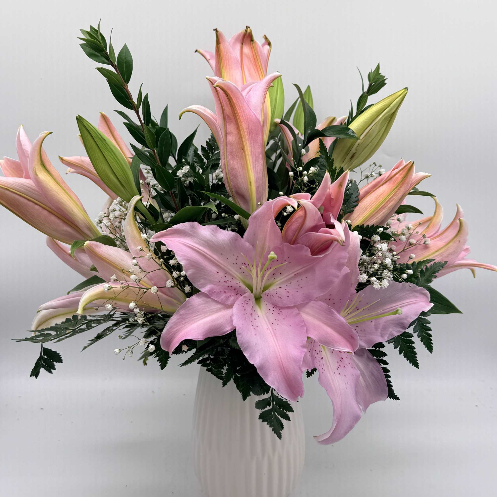 Pink lilies arranged in a white vase with greenery