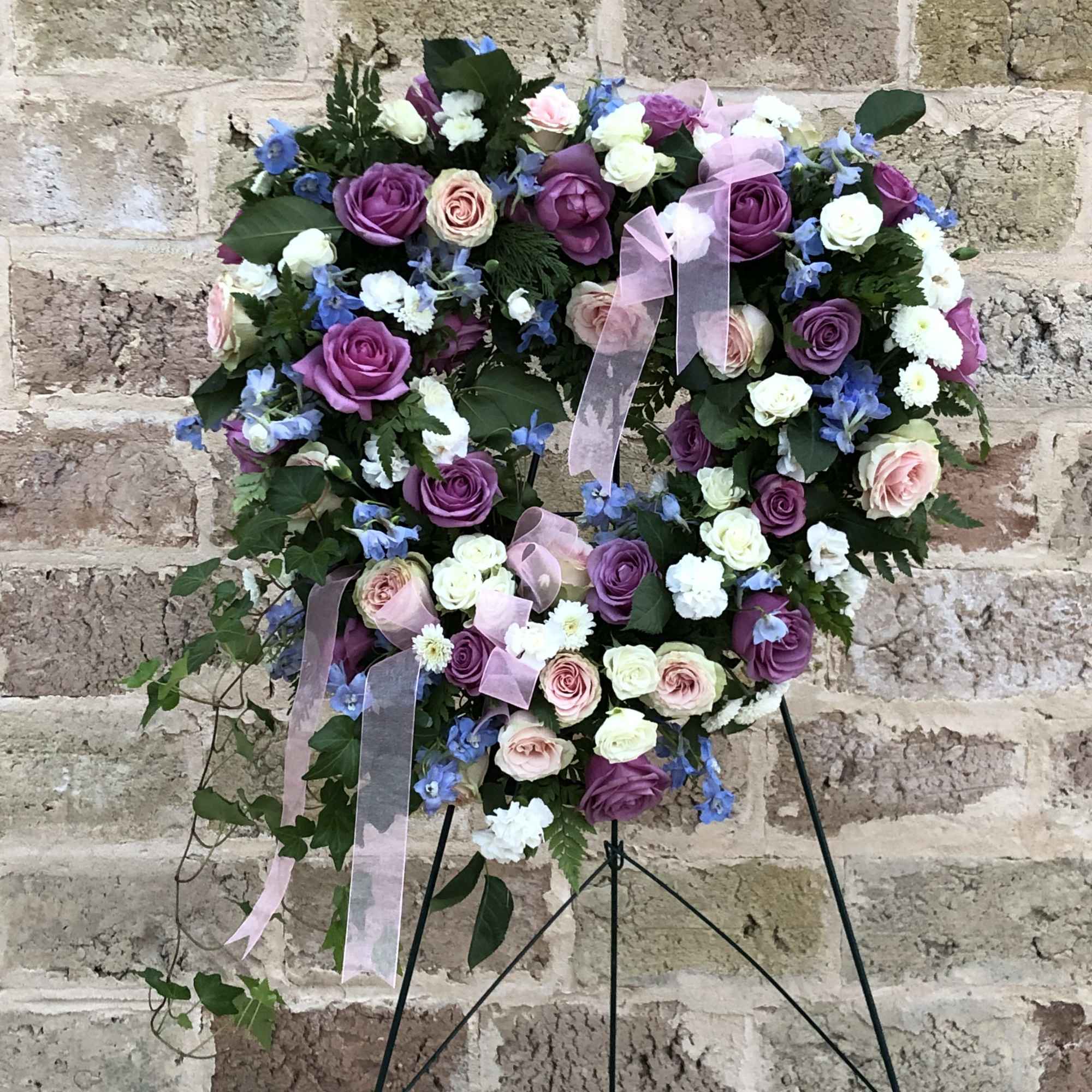 Heart-shaped floral wreath with purple and pink roses on a stand