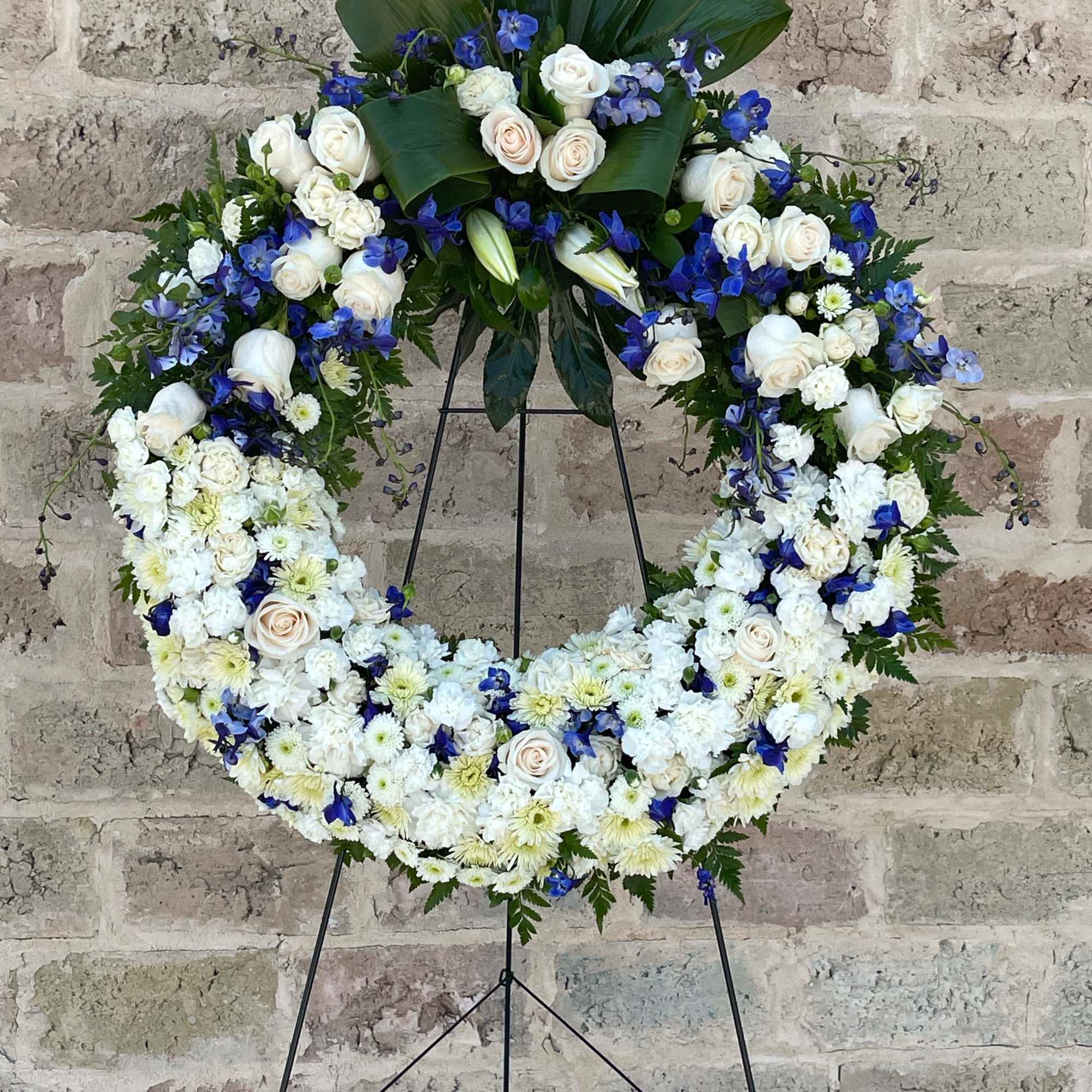 Large white and blue floral wreath on a black stand