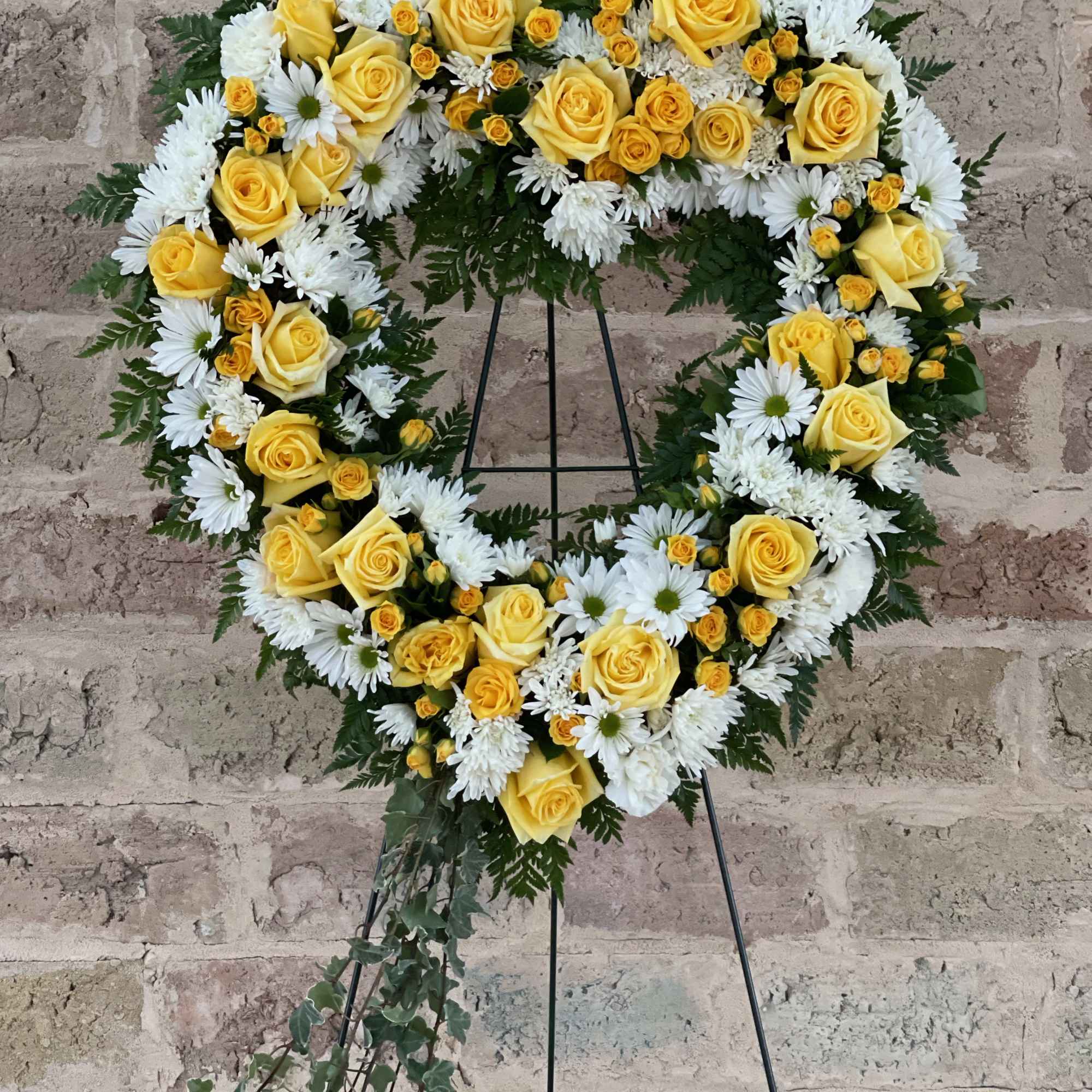 Heart-shaped floral wreath of yellow roses and white daisies on a stand
