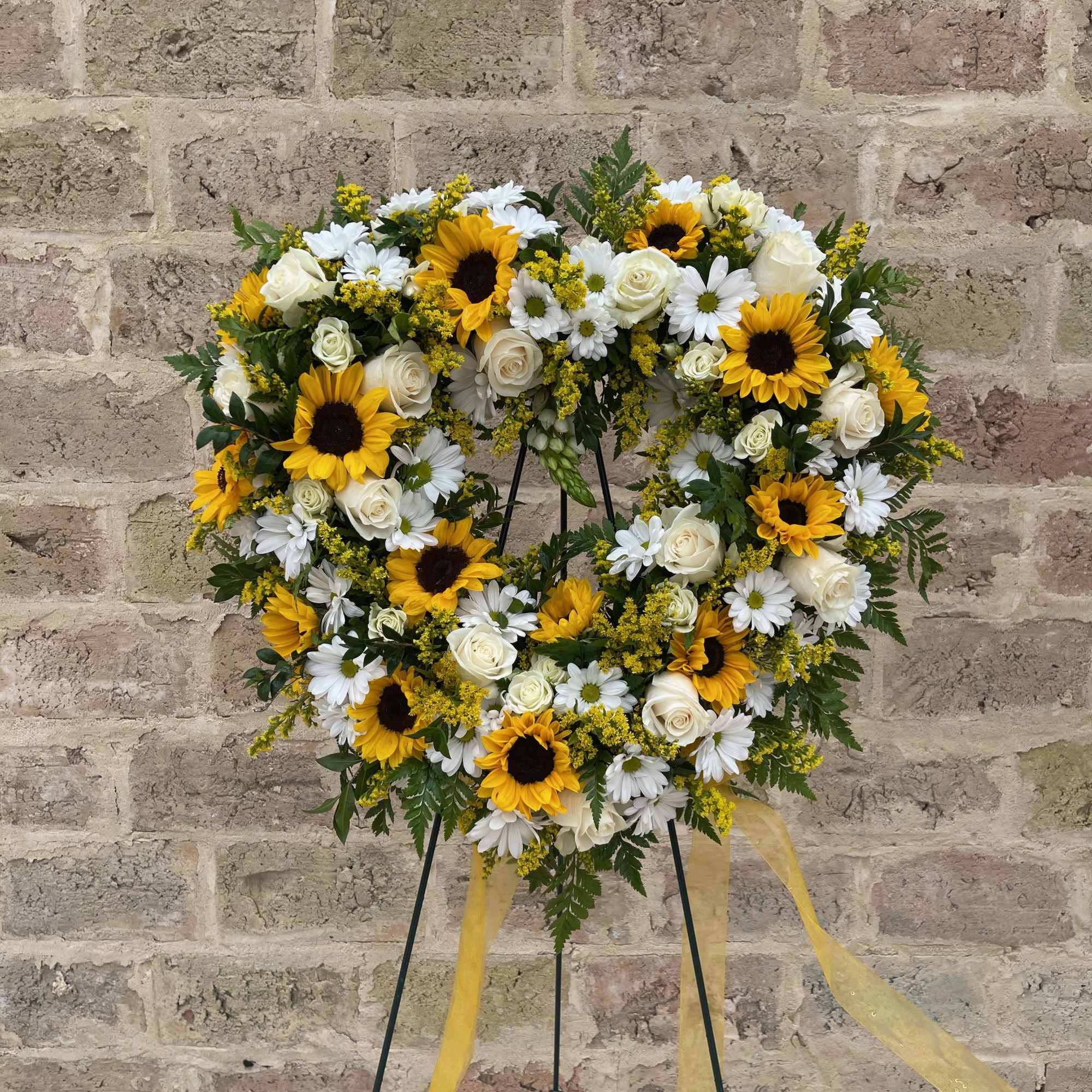 Heart-shaped floral wreath with sunflowers, white roses, and daisies on a stand