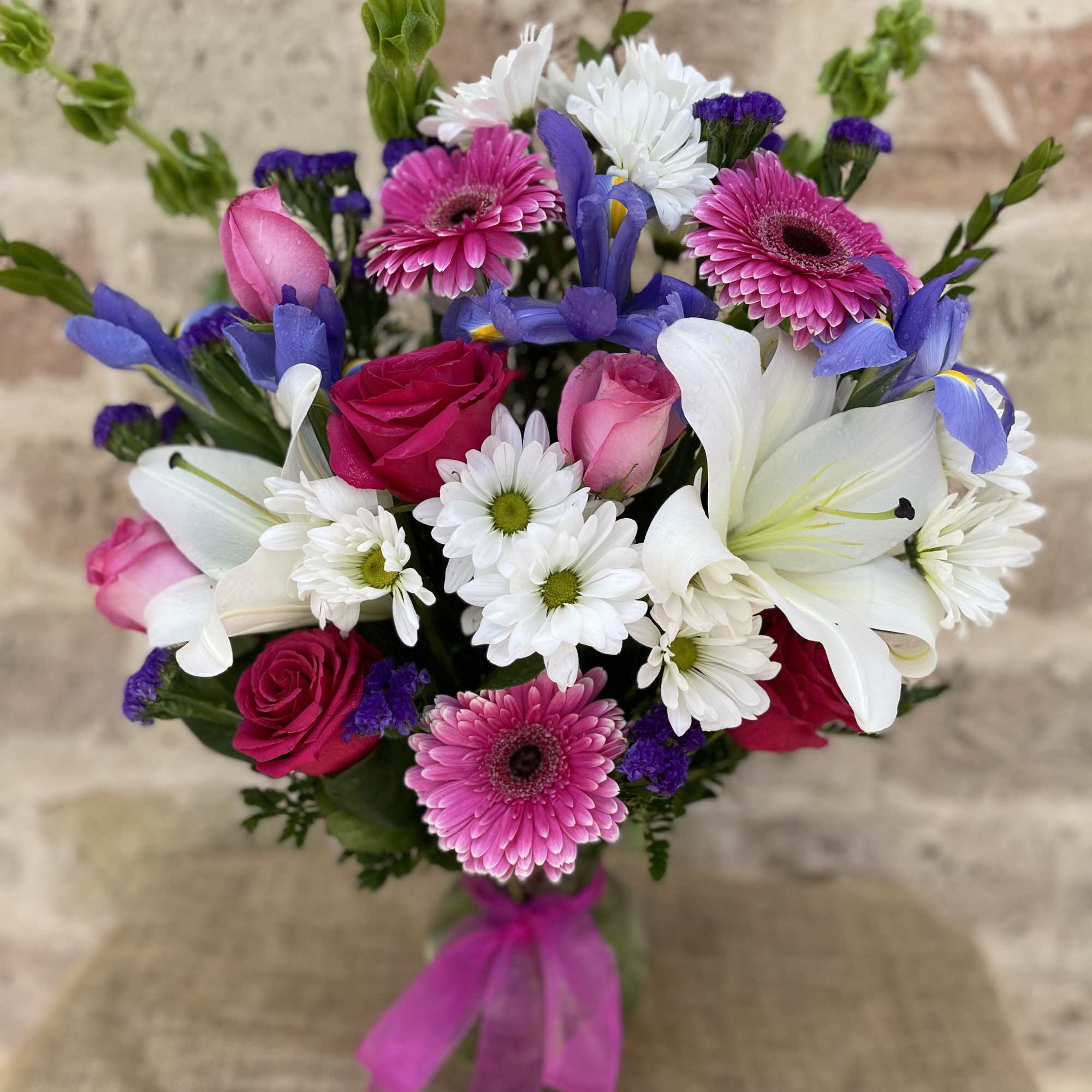 Mixed bouquet with pink roses, white lilies, and purple flowers tied with a pink ribbon