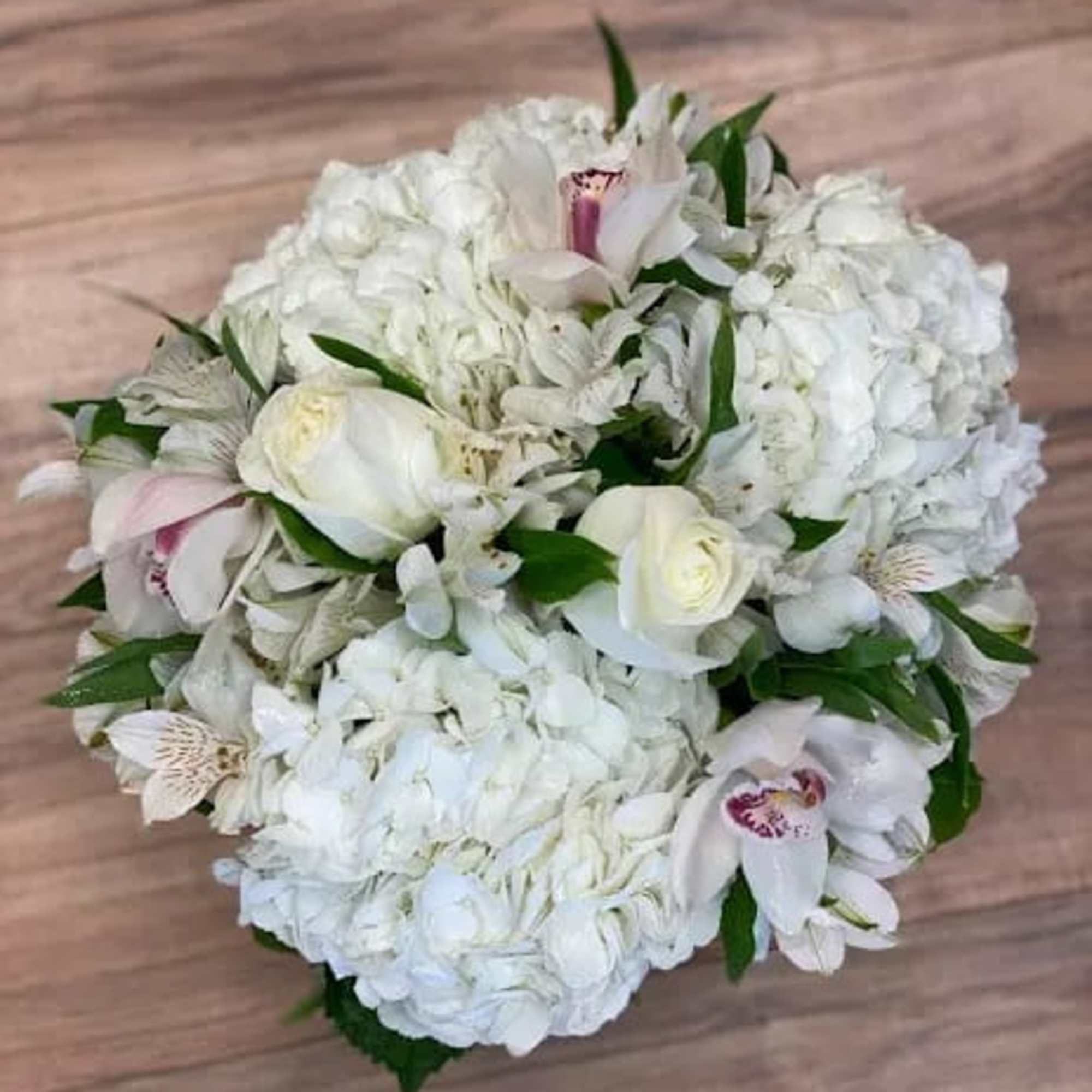 White bouquet with hydrangeas, roses, and orchids on a wooden surface