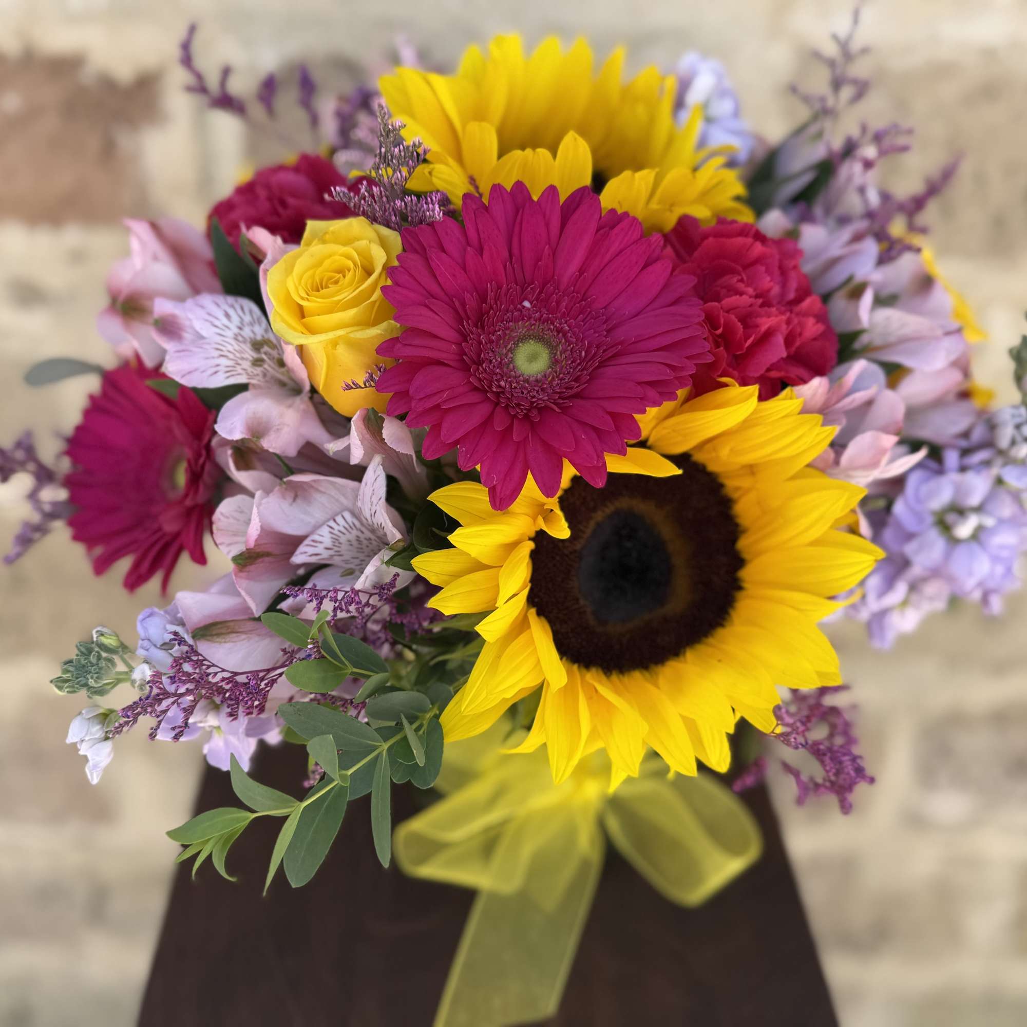 Bouquet of sunflowers, pink gerbera daisies, and purple flowers with a yellow ribbon