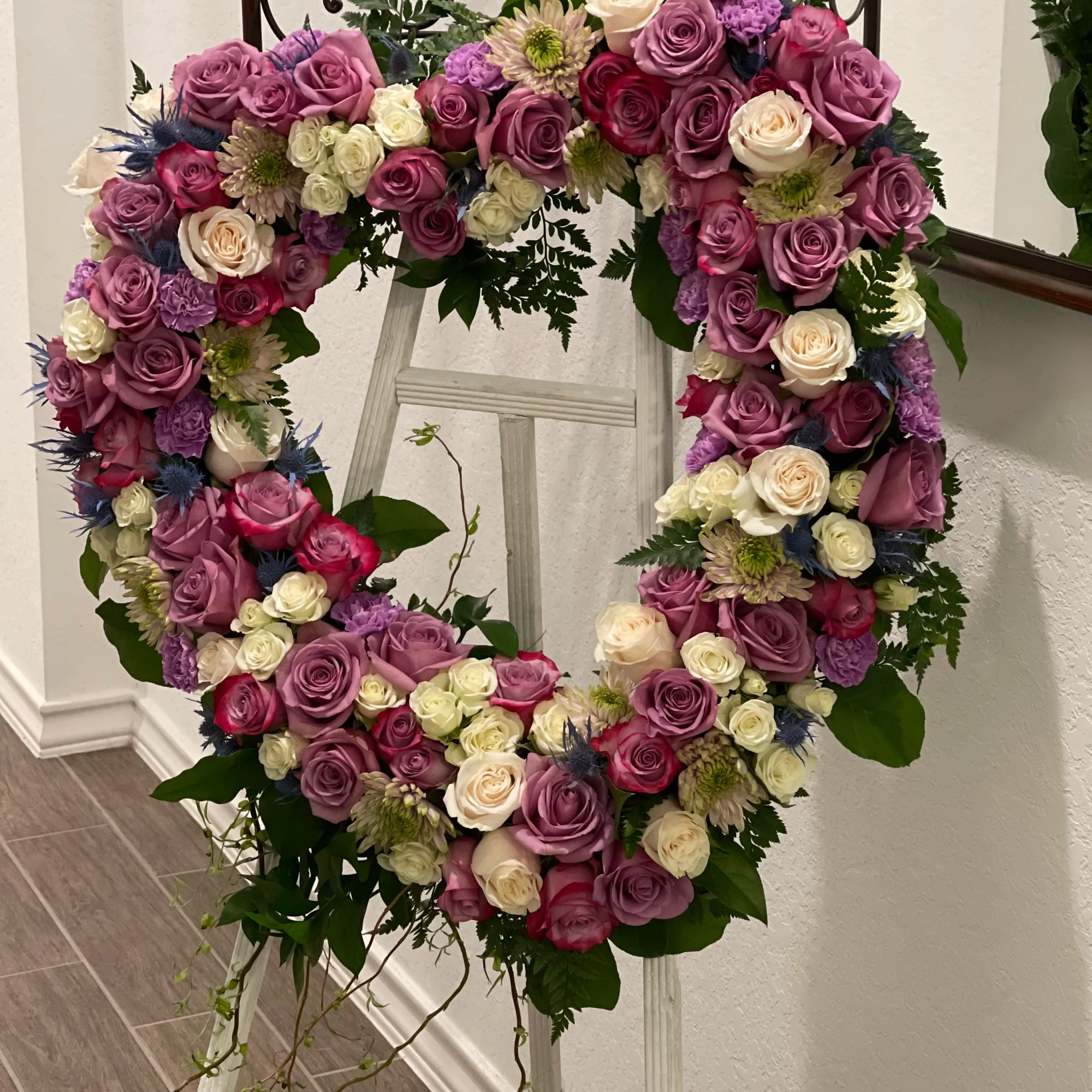 Heart-shaped floral wreath of pink, purple, and white roses on a stand