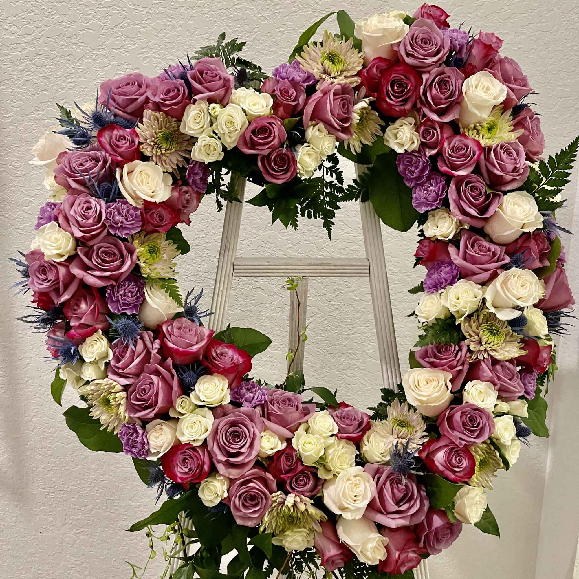 Heart-shaped floral wreath of pink, white, and purple roses on a stand