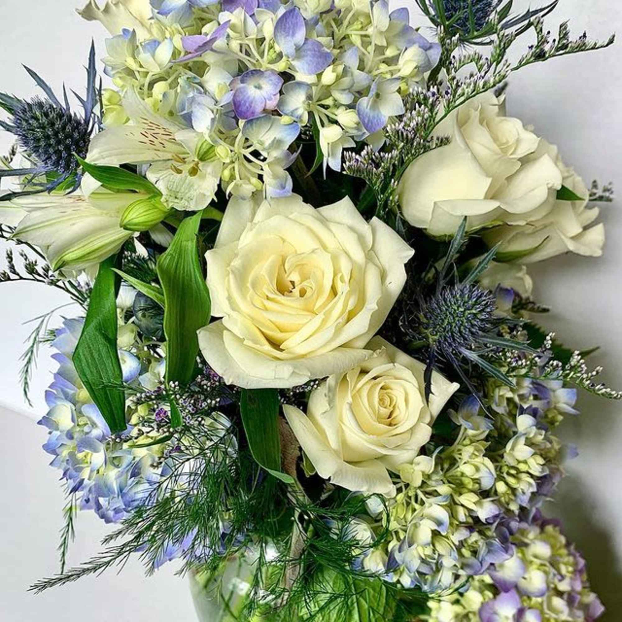 Bouquet of cream roses and pale blue flowers with greenery