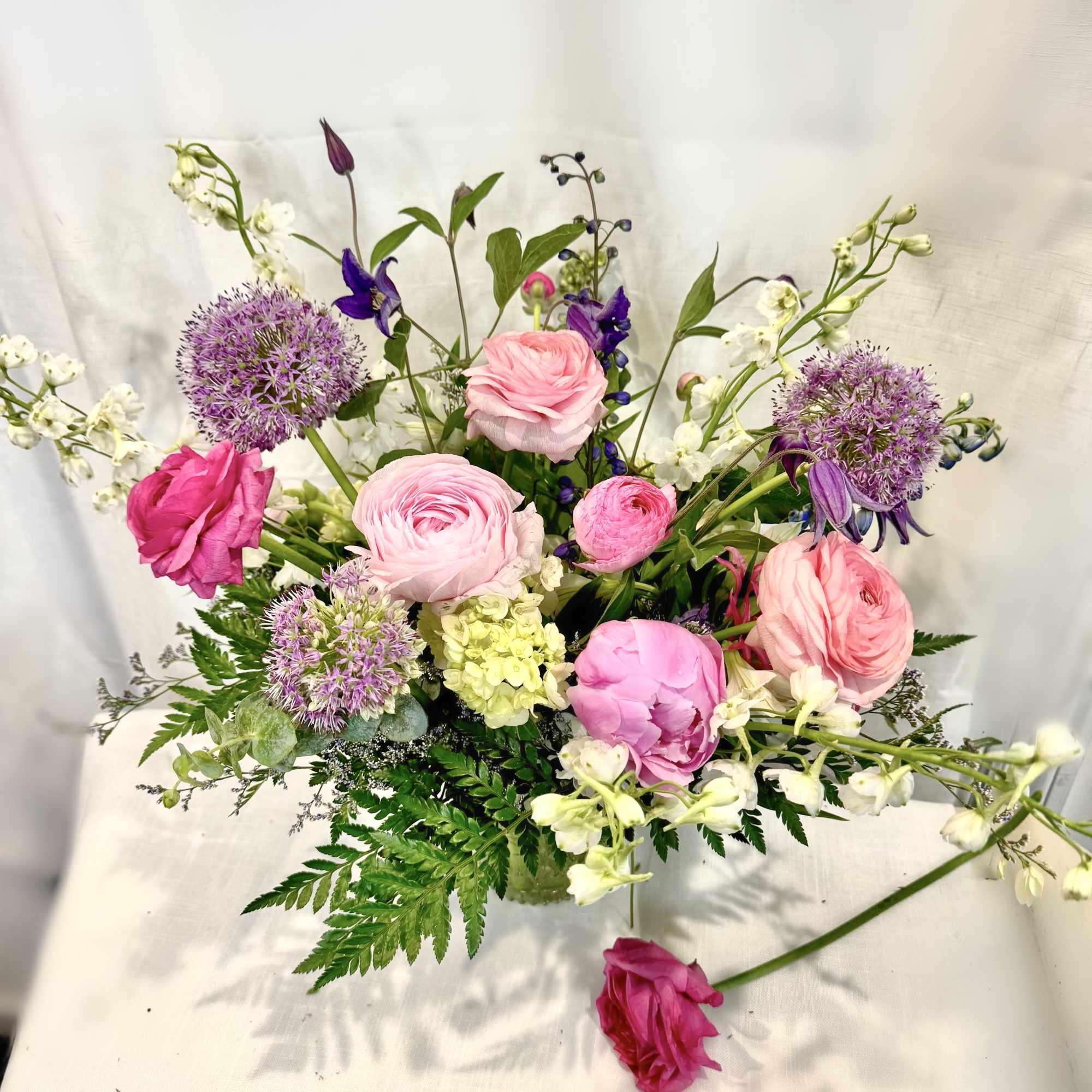 Layered pink ranunculus and roses mingle with tall blue‑purple delphinium and pops