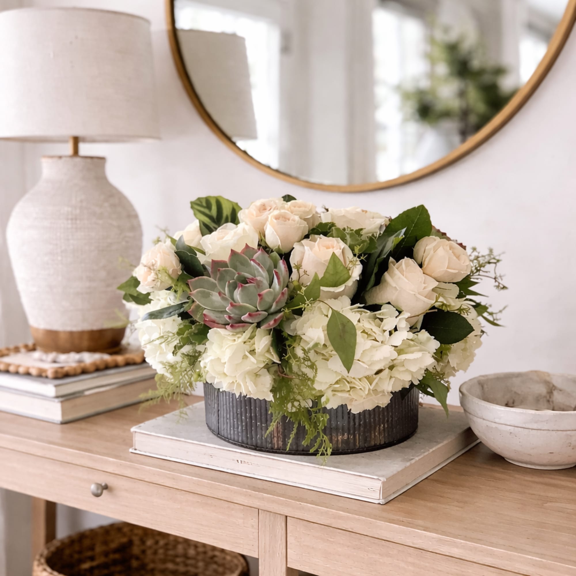 Cream roses and hydrangeas in a low metal container with a succulent center