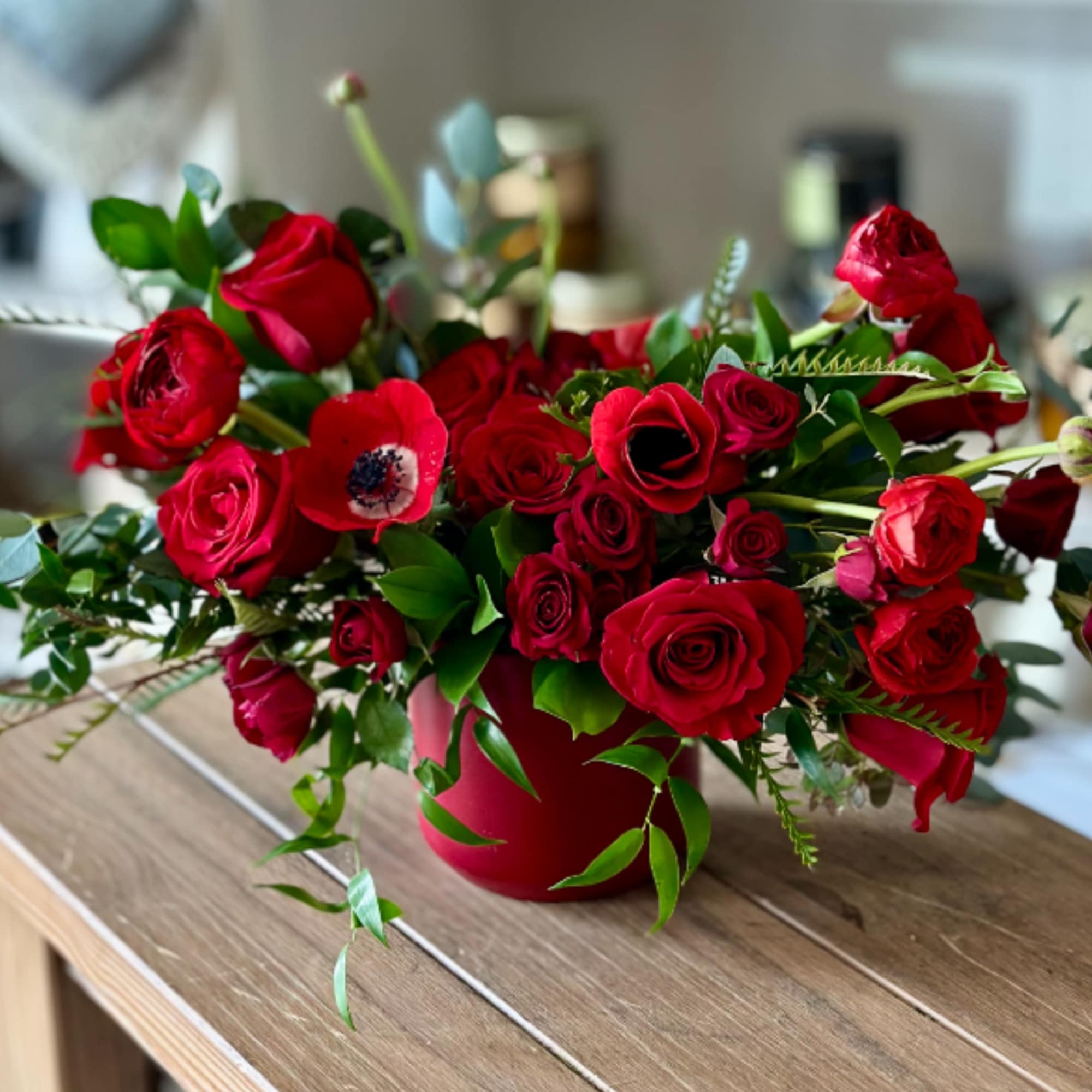 Red roses arranged in a red vase with green foliage