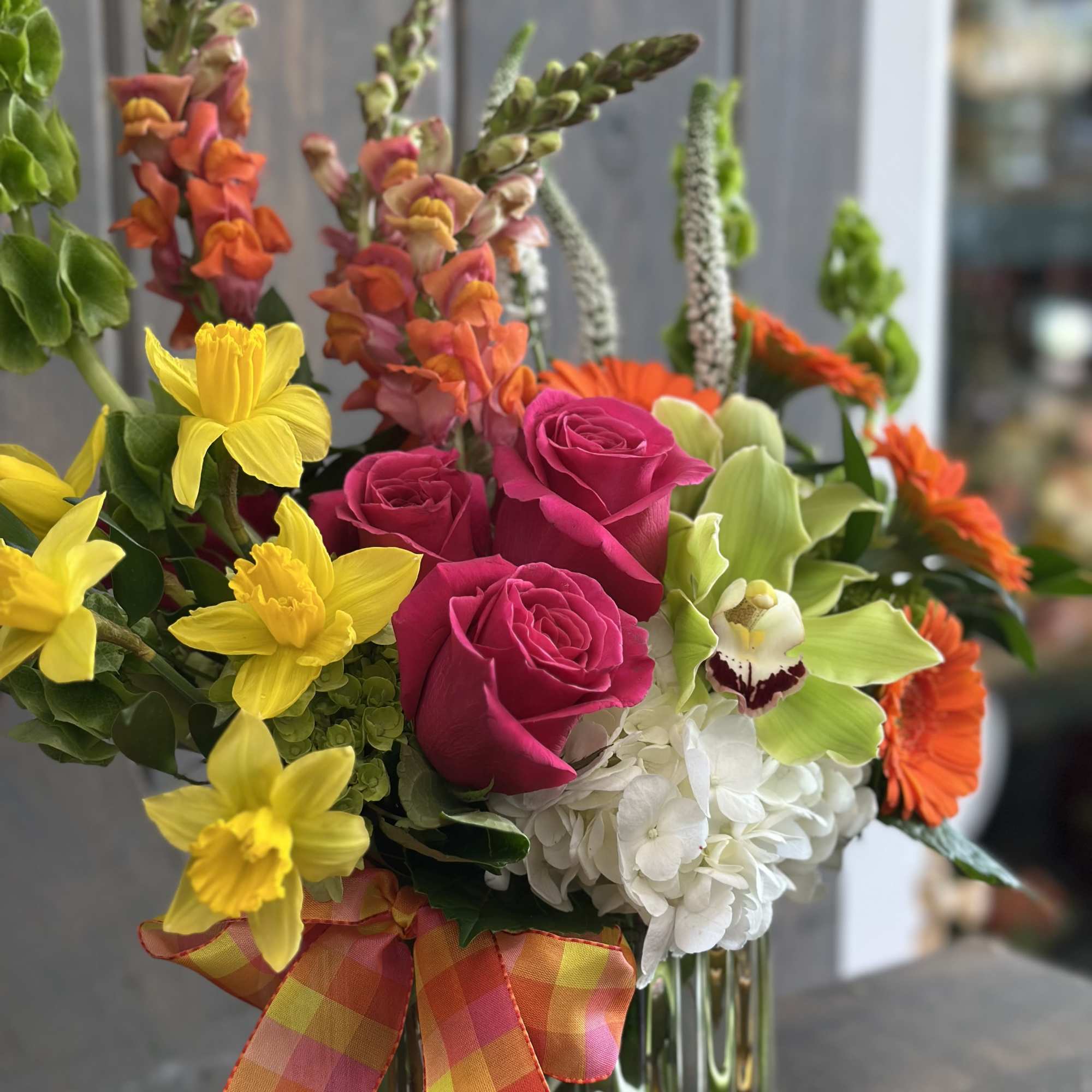 Colorful bouquet of roses, daffodils, orchids, and snapdragons in a glass vase