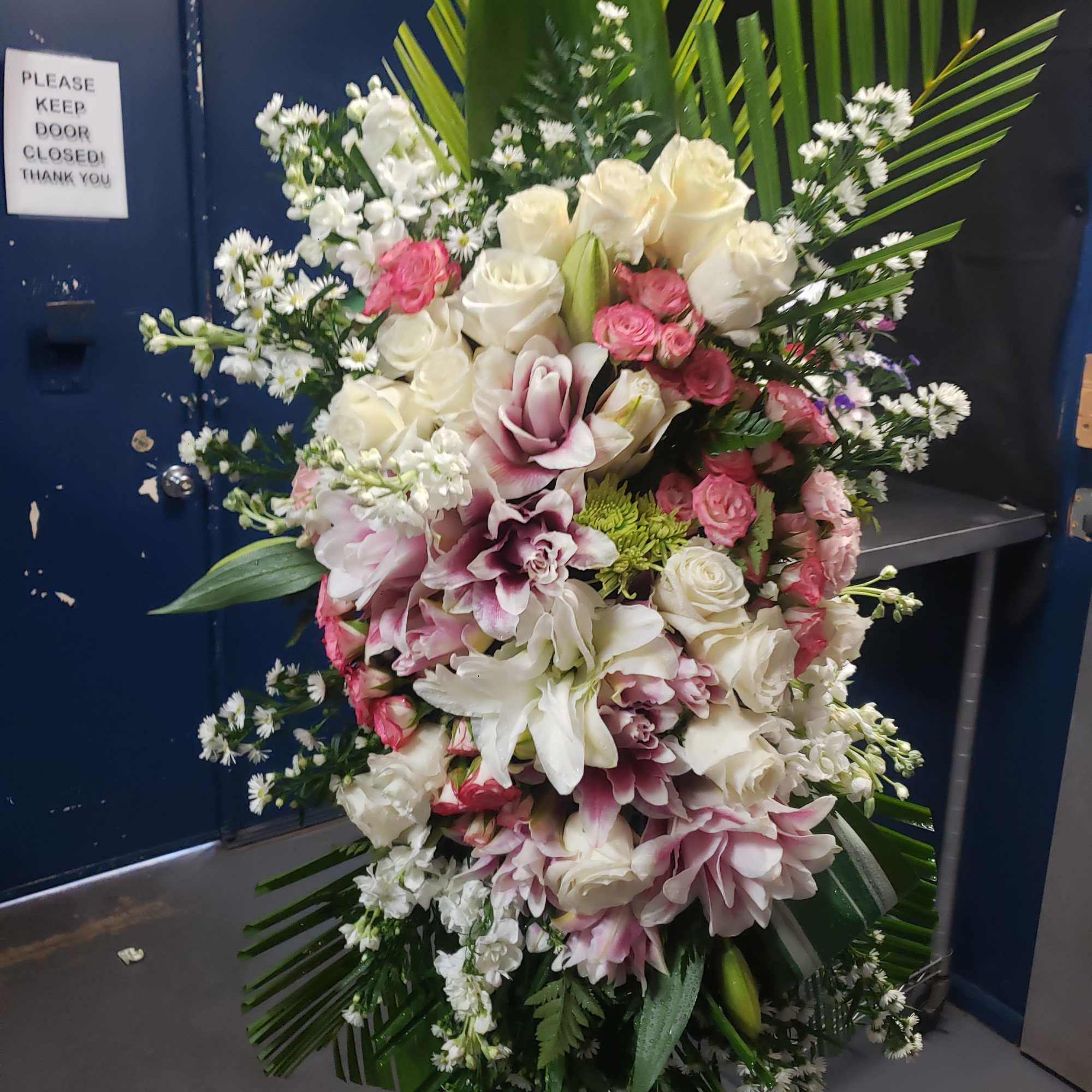 A tall, graceful standing spray of soft pink roses, white lilies, and