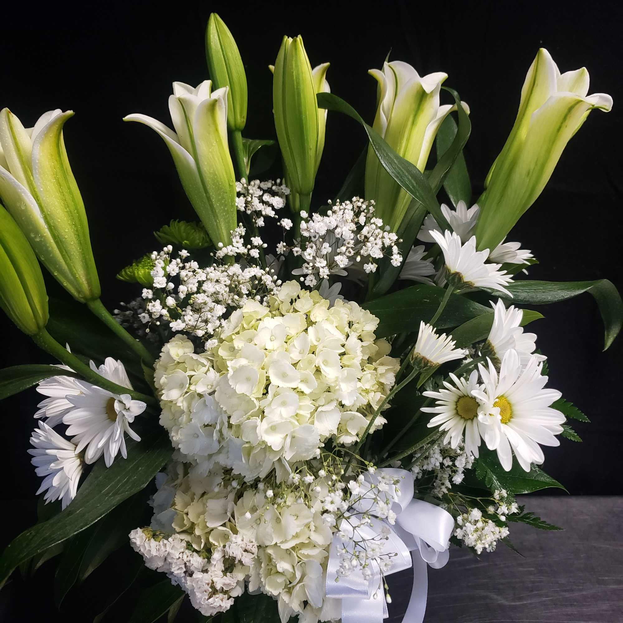 A tall, graceful standing spray of soft pink roses, white lilies, and