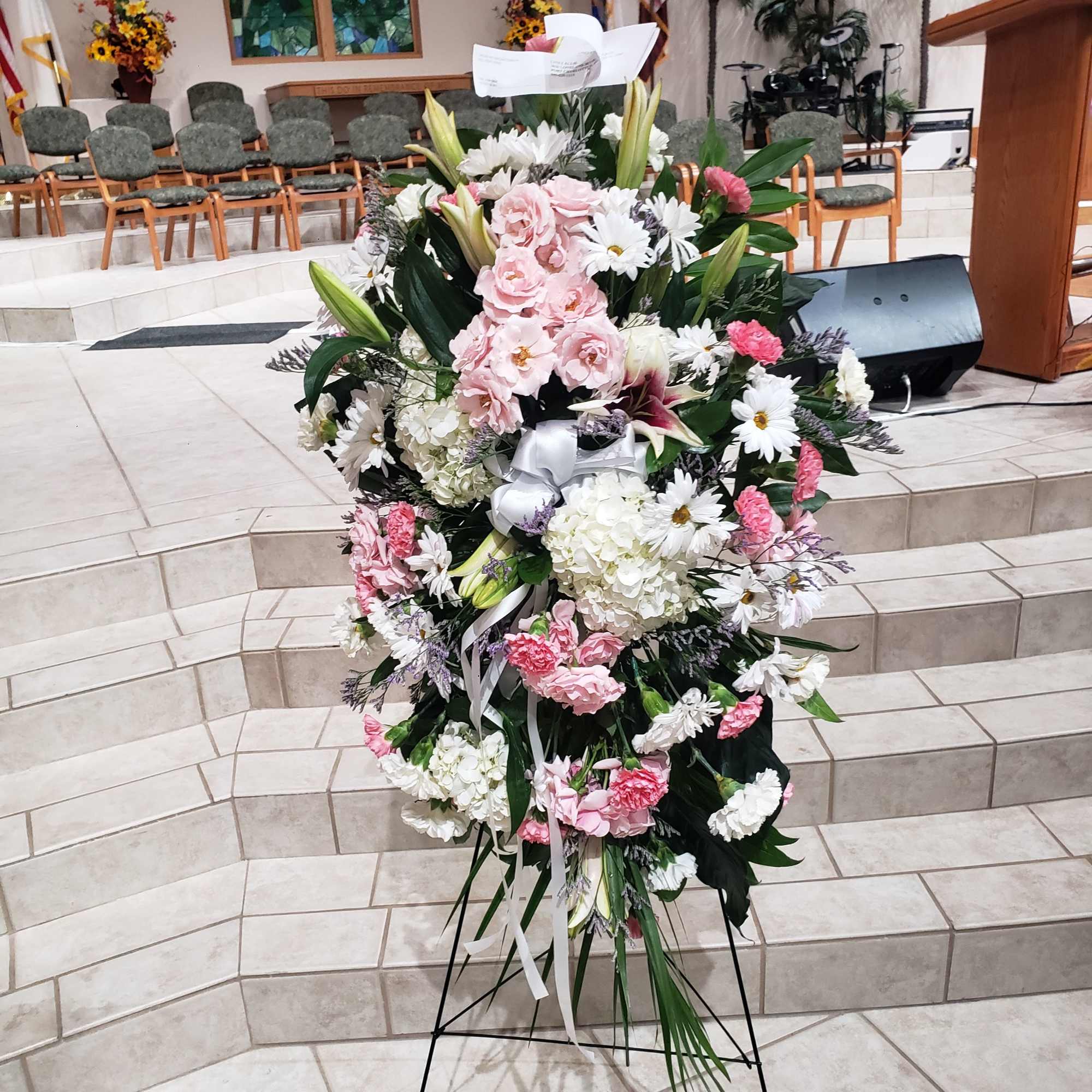 A tall, graceful standing spray of soft pink roses, white lilies, and