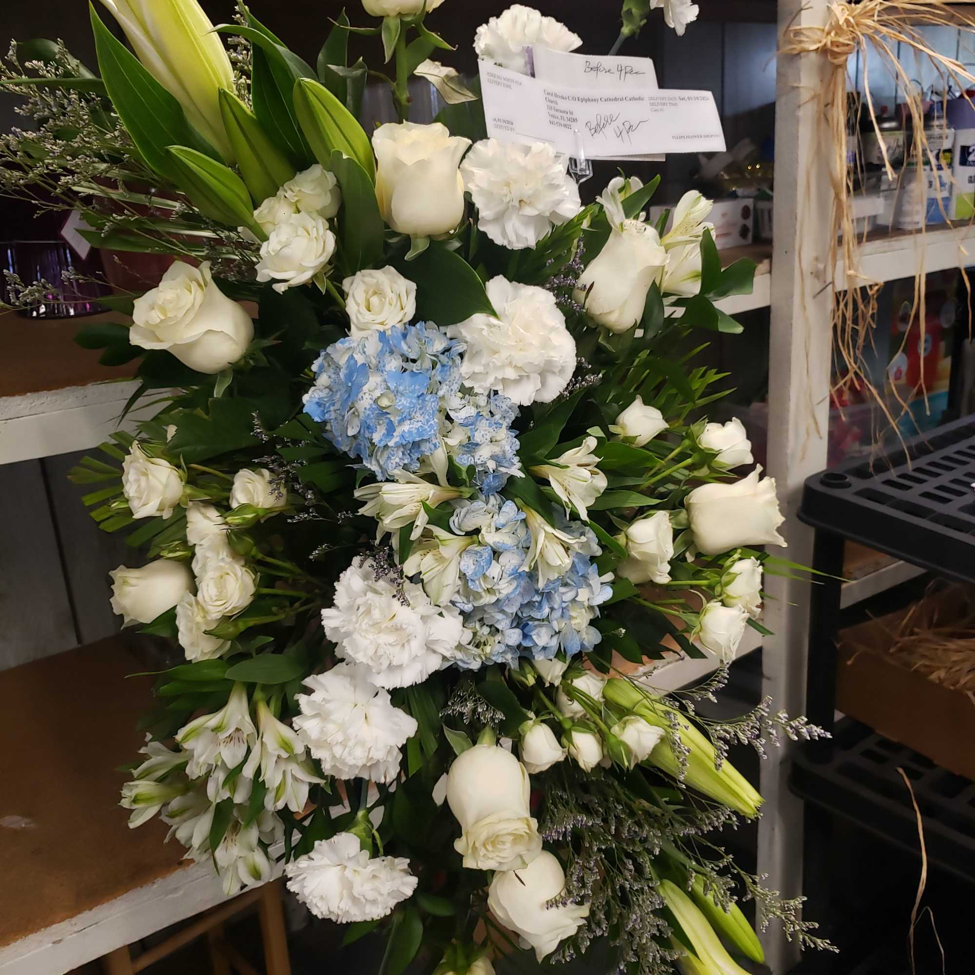 A tall, graceful standing spray of soft pink roses, white lilies, and