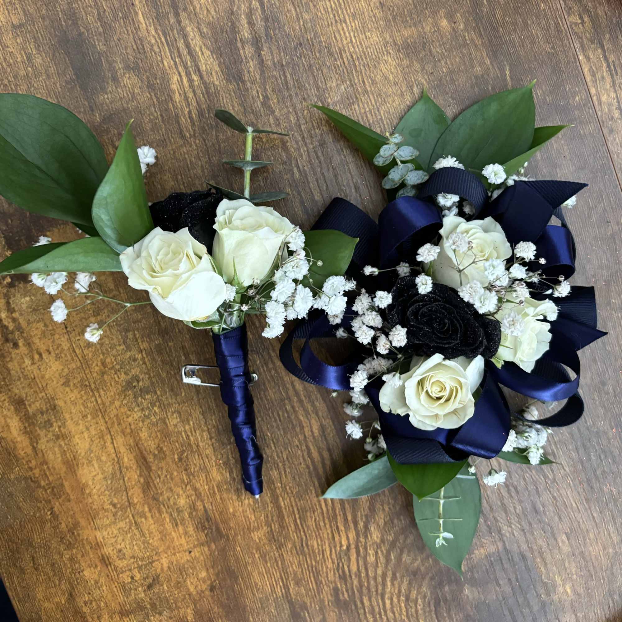 Two floral boutonnieres with white and black roses and navy ribbon