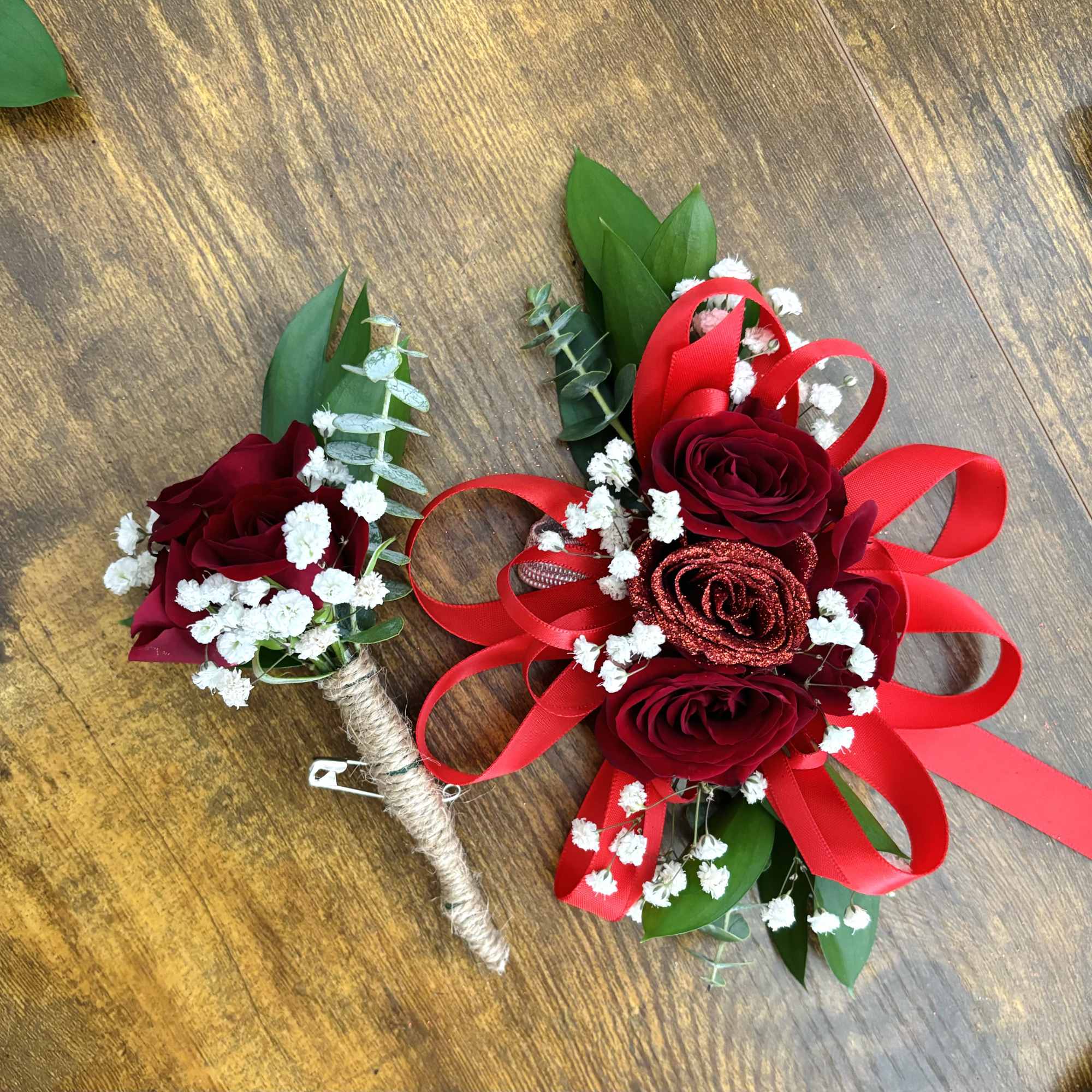 Two red rose boutonnieres with baby's breath and ribbon accents