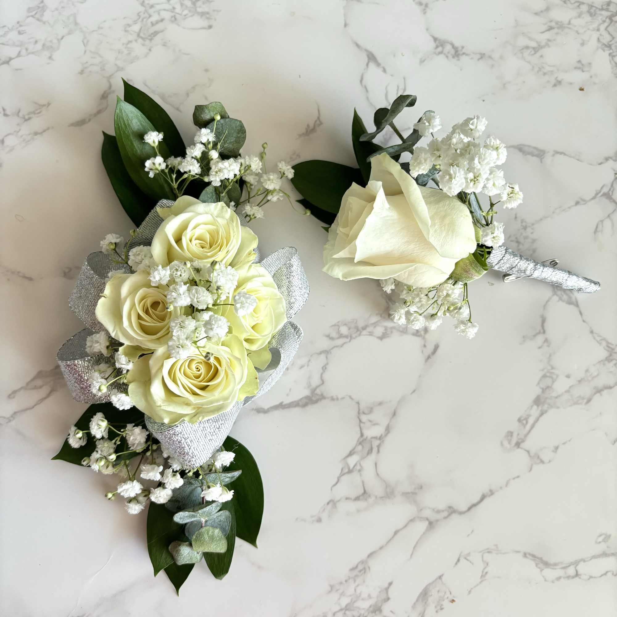 Two white rose boutonnieres with baby's breath and silver ribbon